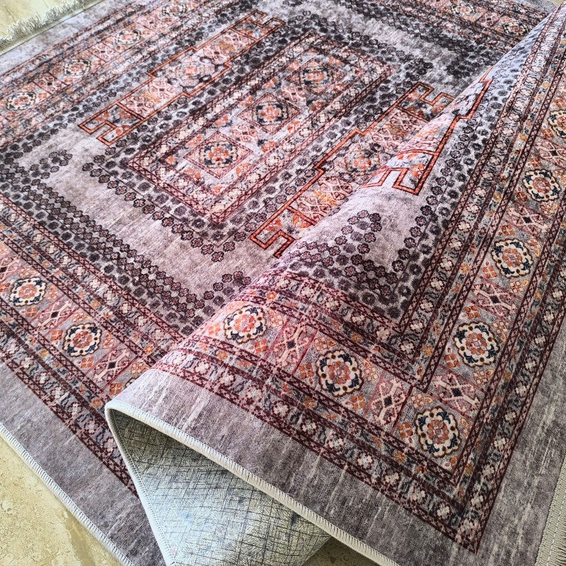 Tapis velouté aux motifs floraux et géométriques complexes dans des tons gris, bordeaux, orange et crème, avec un bord roulé