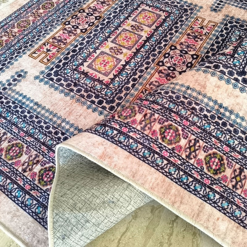 Tapis à motifs orientaux beiges, bleus, roses et jaunes. La surface veloutée du tapis est partiellement roulée, exposant son envers gris antidérapant