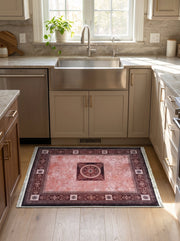 Tapis rectangulaire rose délavé à motifs bordeaux élaborés, avec une bordure et un médaillon central, posé sur le sol en bois d'une cuisine lumineuse