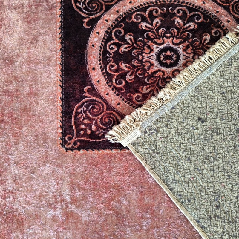 Tapis rose pelucheux, avec un tapis bordeaux à motifs orange, dont l'envers beige quadrillé et les franges sont visibles