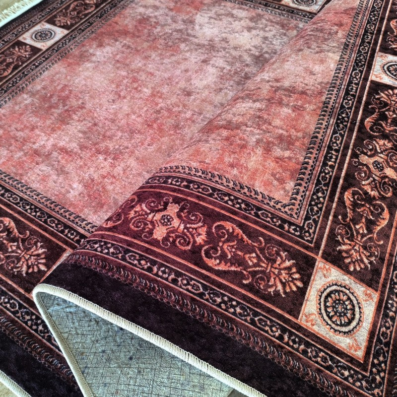 Tapis rose corail texturé à large bordure marron foncé ornée de motifs classiques, en partie roulé