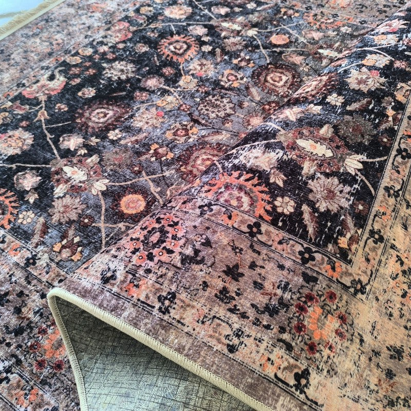 Tapis floral aux motifs ornementaux, teintes de noir, gris, brun, orange rouille et beige, avec un aspect vieilli