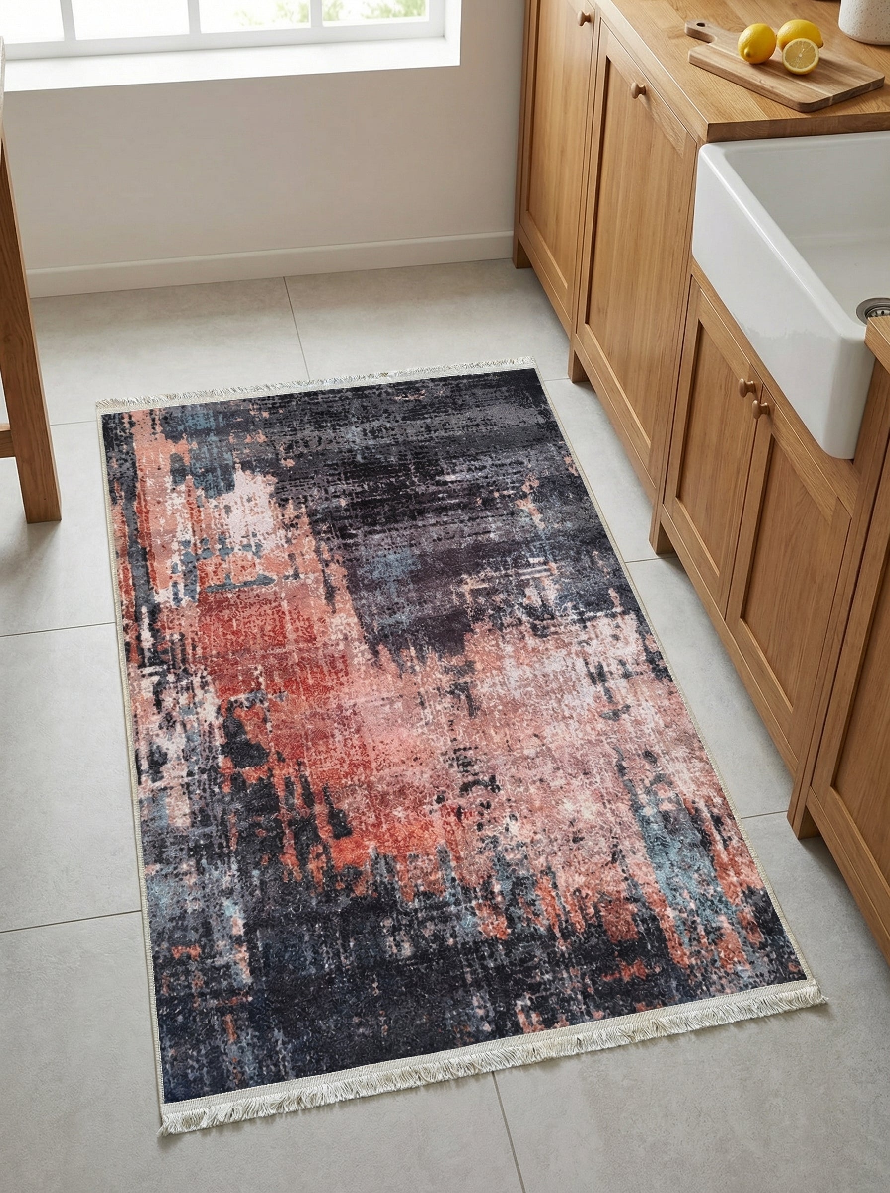 Tapis rectangulaire aux motifs abstraits noirs, corail et bleus, avec franges, sur un sol carrelé dans une cuisine moderne