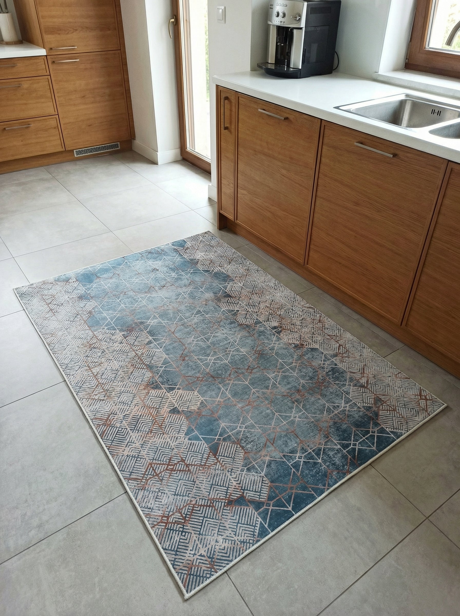 Tapis rectangulaire aux motifs géométriques bleu-vert, beige et cuivrés, sur un sol carrelé clair dans une cuisine