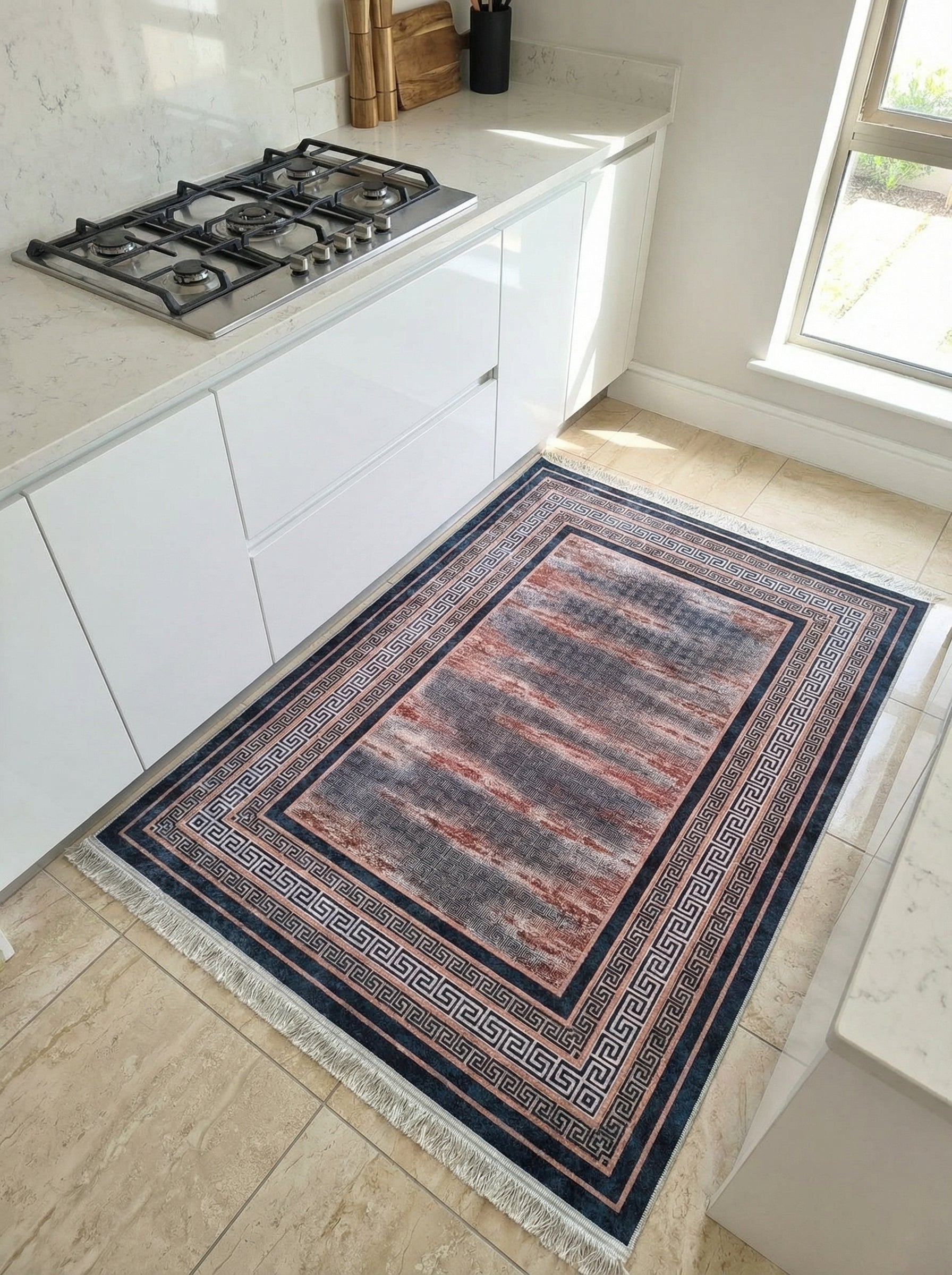 Tapis rectangulaire à franges, centre abstrait gris et rouge terre cuite, bordure à motifs grecs bleu foncé et blanc, dans une cuisine