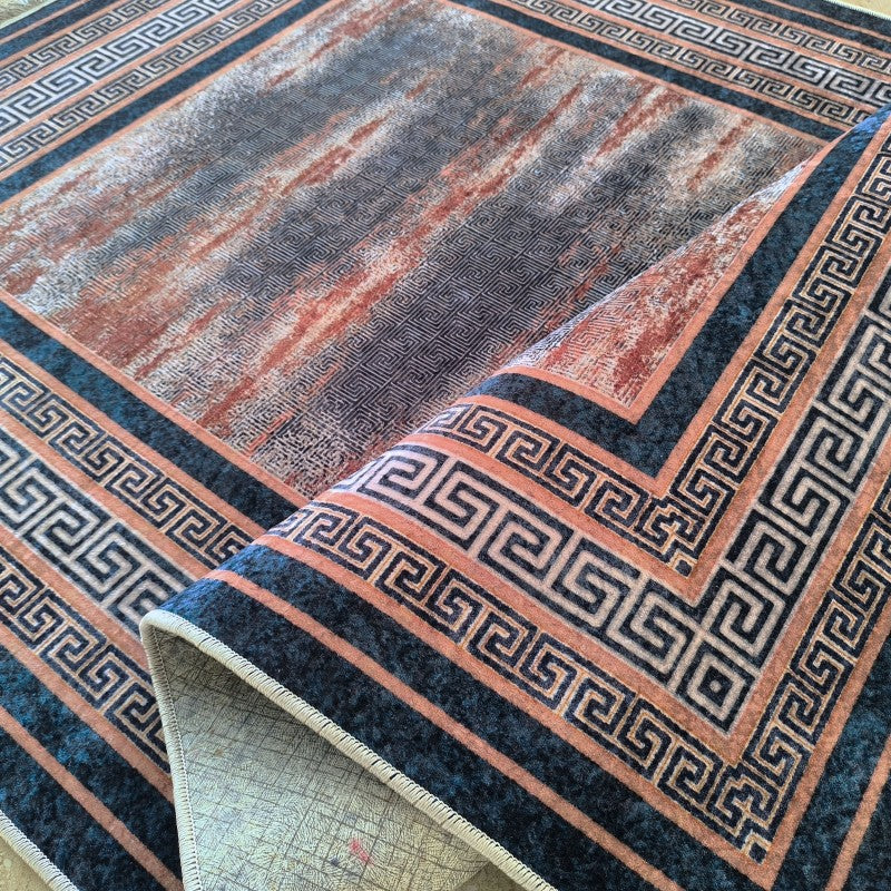 Tapis velouté aux motifs abstraits gris et rouille, bordure à motifs grecs bleu foncé sur fond rouille. Un coin est soulevé