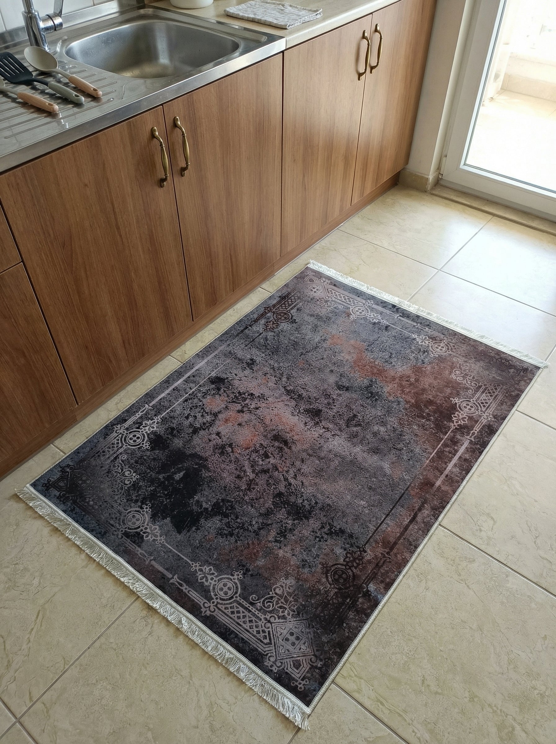 Tapis rectangulaire à franges, gris anthracite marbré de rouille avec des motifs classiques en bordure, dans une cuisine au sol carrelé