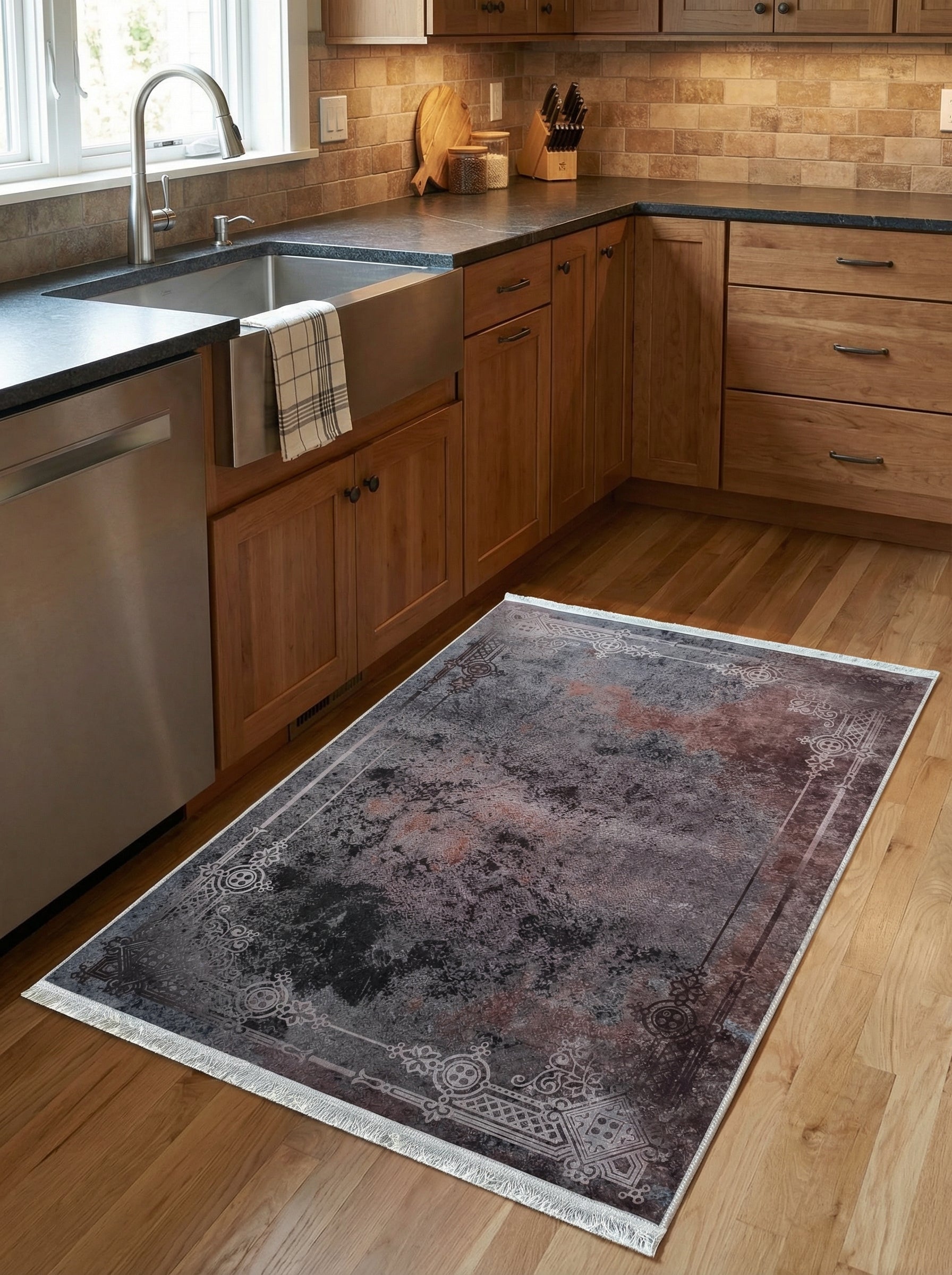 Tapis rectangulaire aux teintes anthracite, rouille et noir, avec motif abstrait et bordure ornée de franges, sur le plancher d'une cuisine