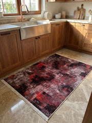 Tapis rectangulaire abstrait aux motifs rouges bordeaux, noirs et blancs effet vieilli, avec franges, posé sur un sol carrelé dans une cuisine