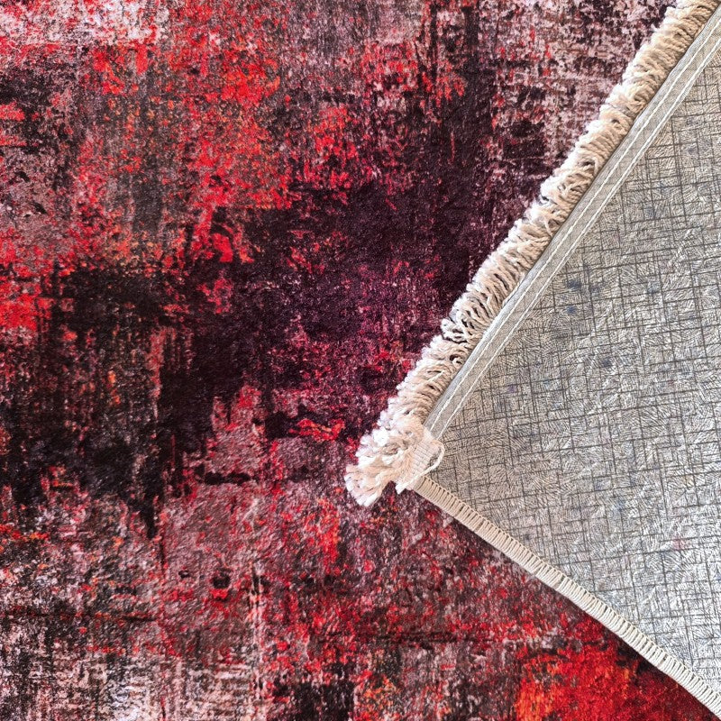 Tapis textile à motifs abstraits rouges, noirs et bordeaux, avec le dos gris à texture quadrillée et des franges crème