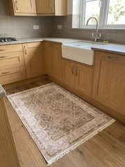 Tapis rectangulaire beige rosé aux motifs floraux bruns et bordure dorée avec franges, posé sur le parquet d'une cuisine