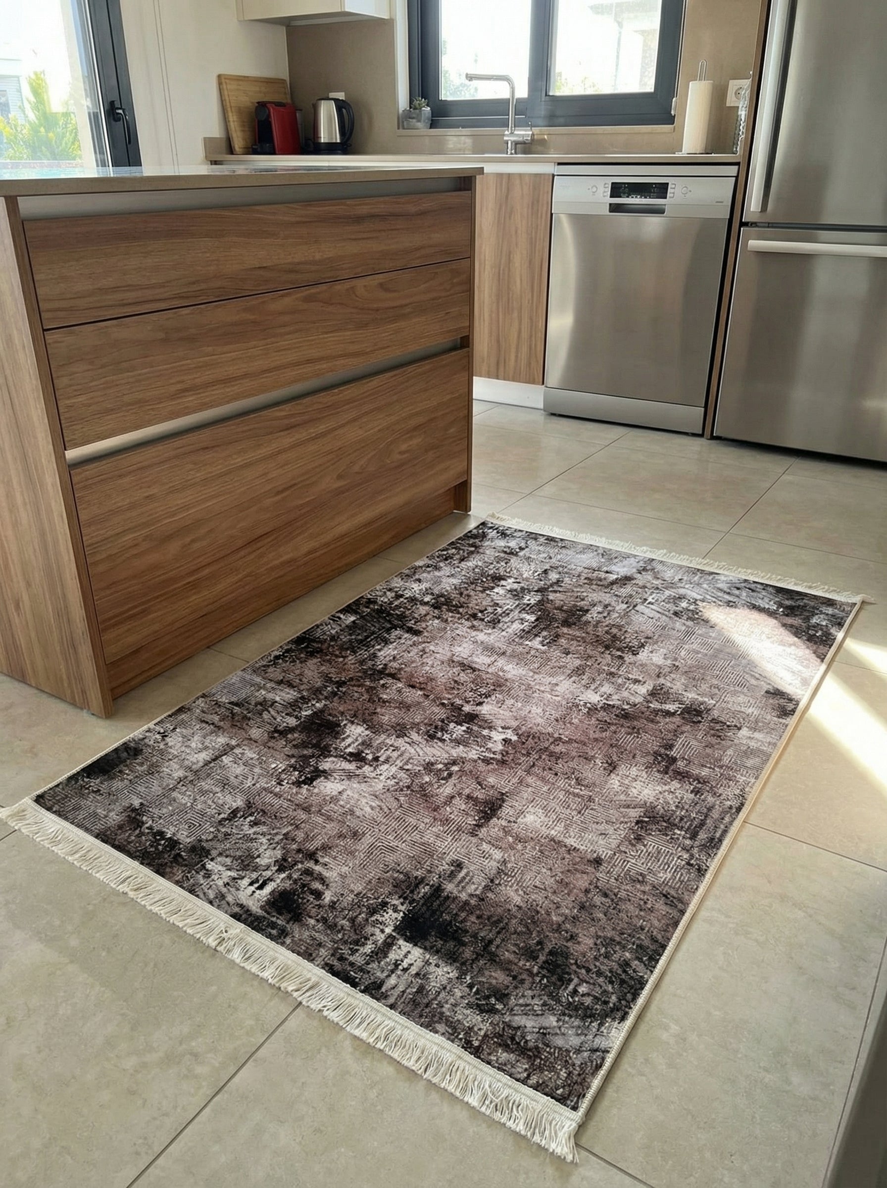 Tapis rectangulaire aux motifs abstraits marron foncé, gris et noir, avec des franges crème, posé sur le carrelage clair d'une cuisine moderne