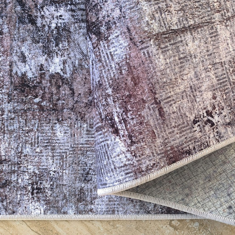 Tapis à la texture douce, motifs abstraits gris, bruns et crème, avec un aspect vieilli, partiellement roulé