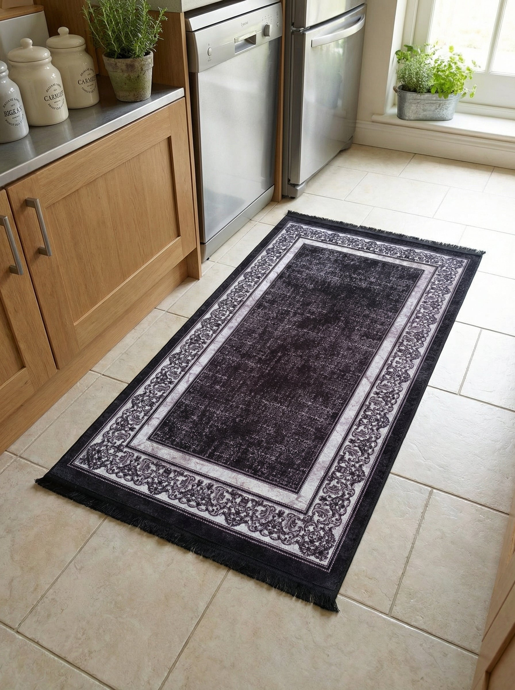 Tapis de passage rectangulaire noir à l'aspect vieilli, orné d'une large bordure d'arabesques blanches et grises, frangé, posé sur un carrelage clair dans une cuisine