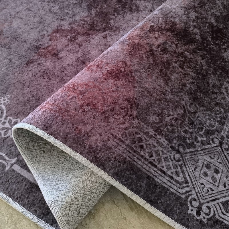 Tapis velouté aux motifs gris clair sur fond dégradé anthracite et bordeaux, enroulé pour montrer l'envers texturé