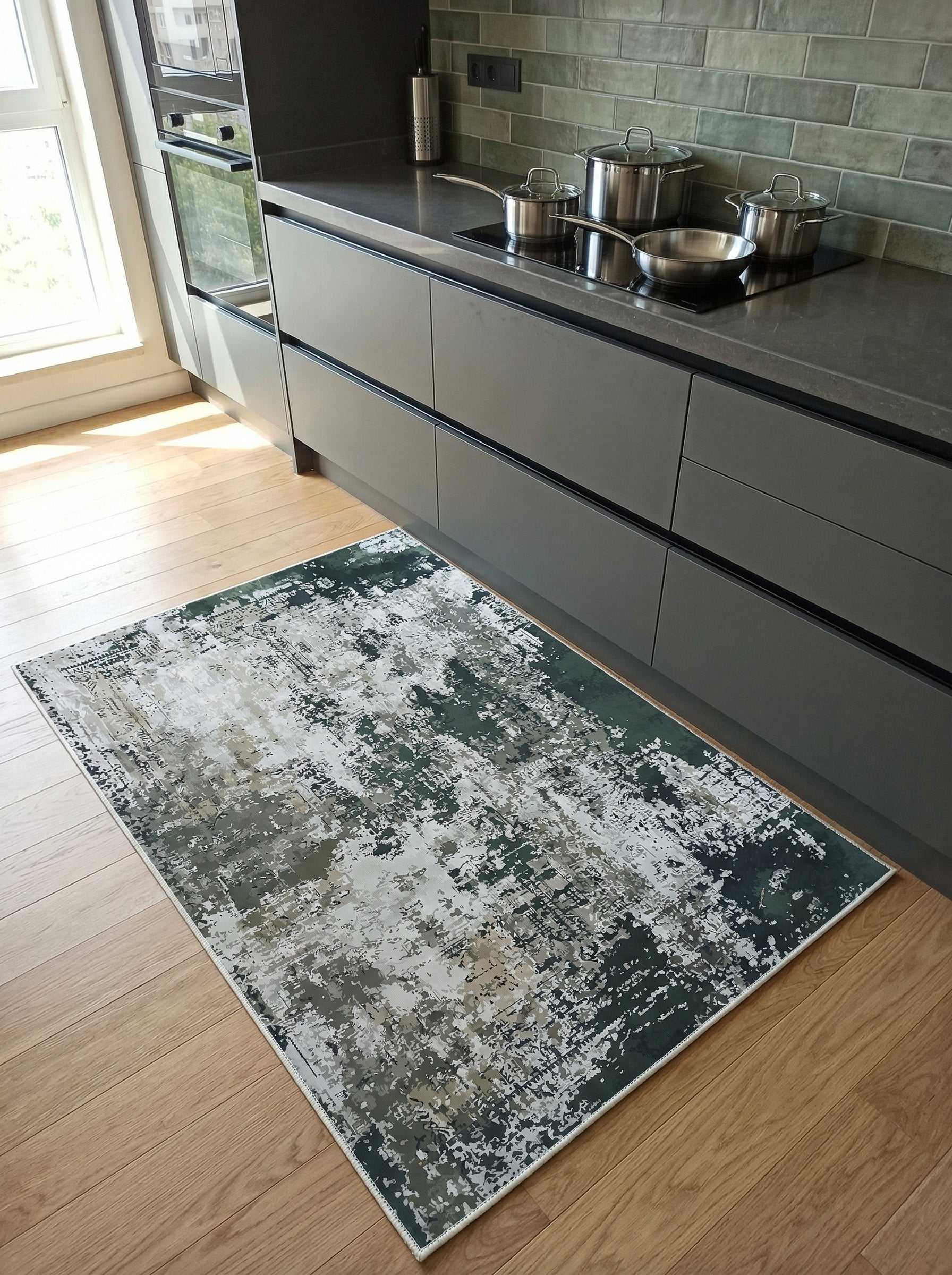Tapis rectangulaire à motif abstrait usé, vert foncé, blanc cassé et gris, posé sur un plancher en bois dans une cuisine moderne