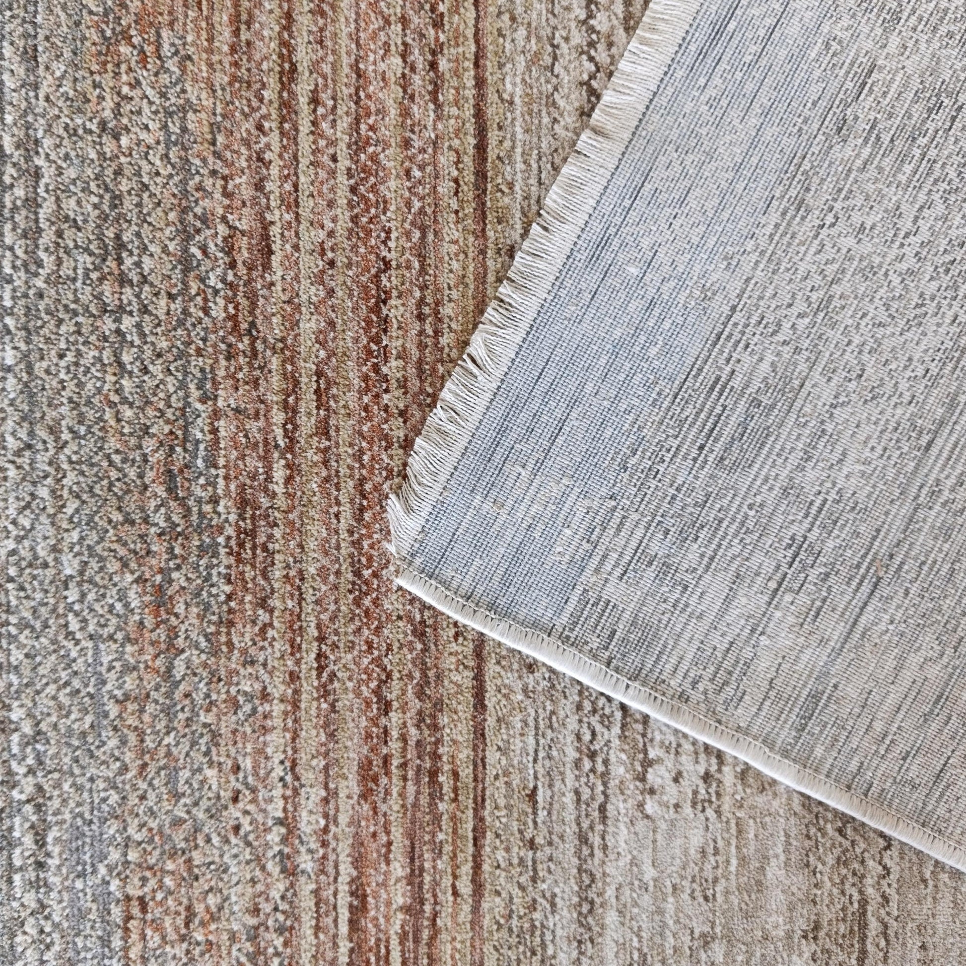 Tapis à poils aux bandes colorées marron, beige et gris, un coin soulevé révèle l'envers tissé clair et des franges courtes