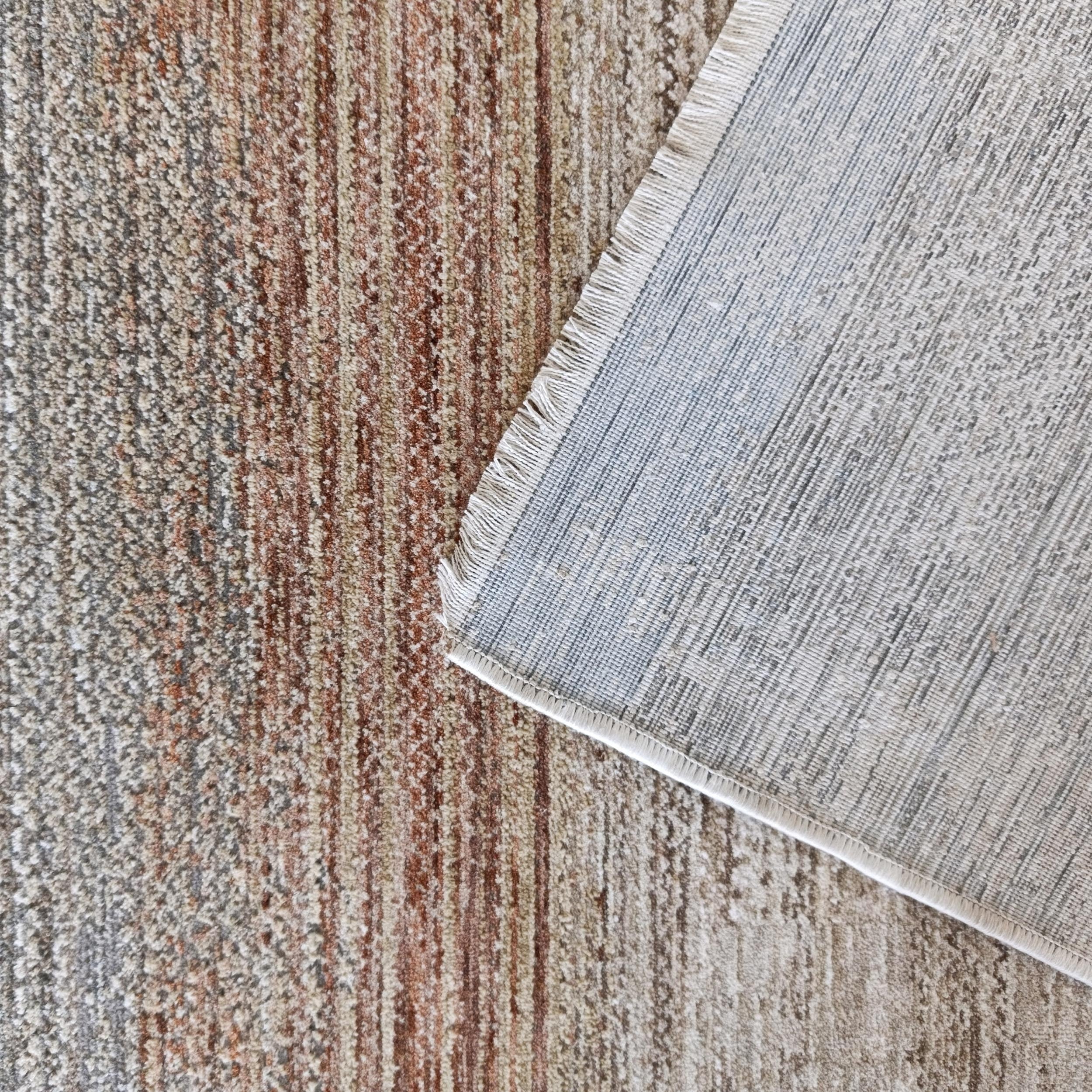 Tapis à poils aux bandes colorées marron, beige et gris, un coin soulevé révèle l'envers tissé clair et des franges courtes
