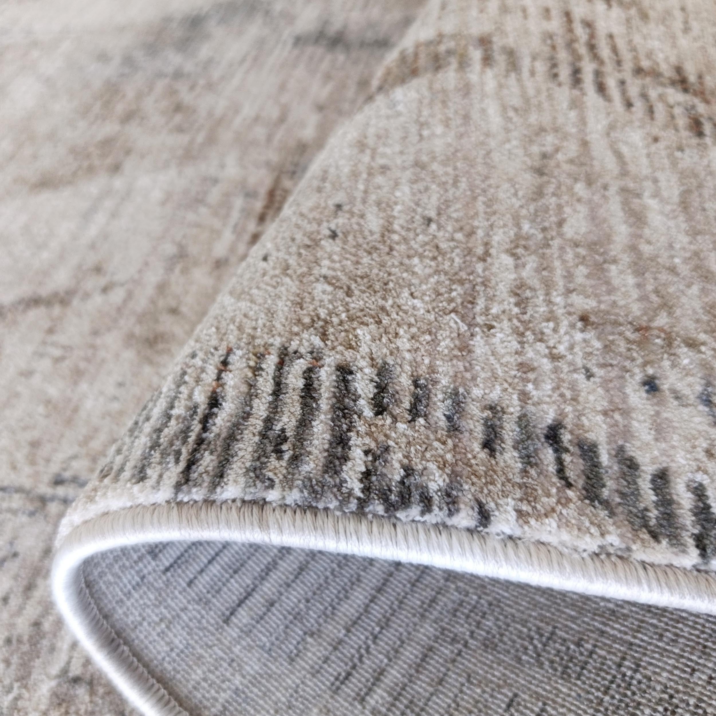 Tapis beige à motifs abstraits gris-marron, doux, roulé, montrant envers gris tissé et bord blanc cousu