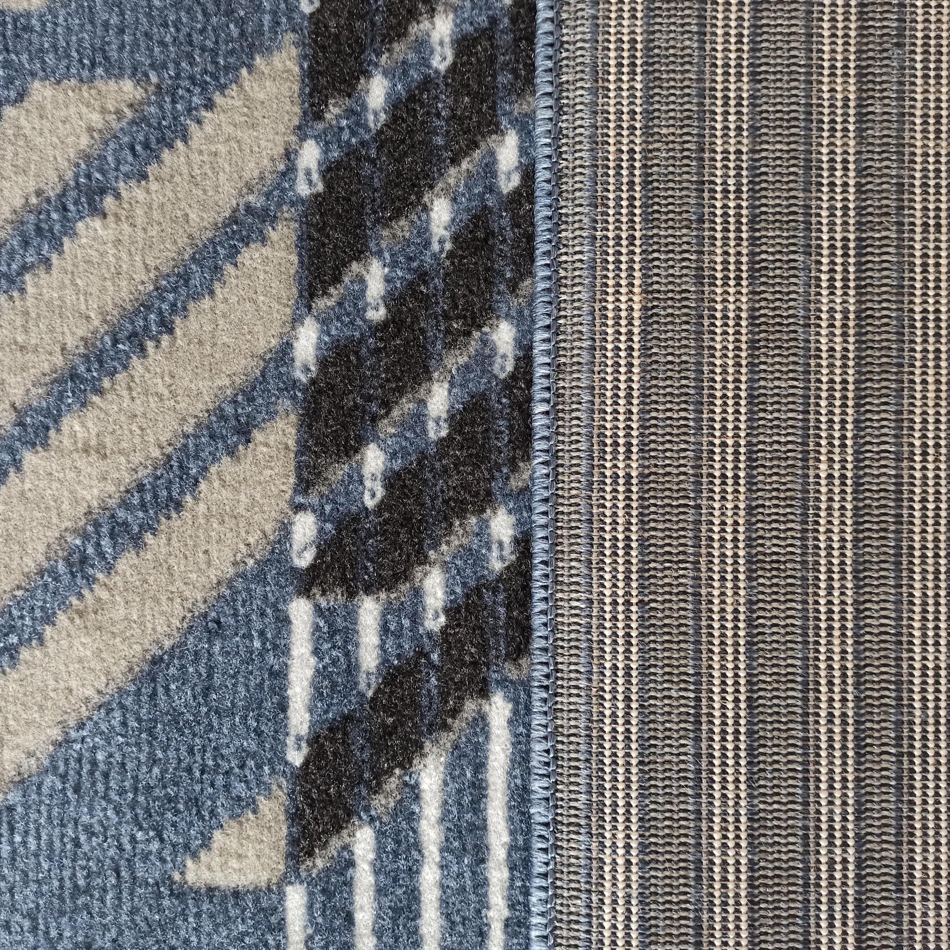 Tapis avec une face veloutée à motifs bleus, beiges et noirs, un envers tissé à rayures grises et blanches
