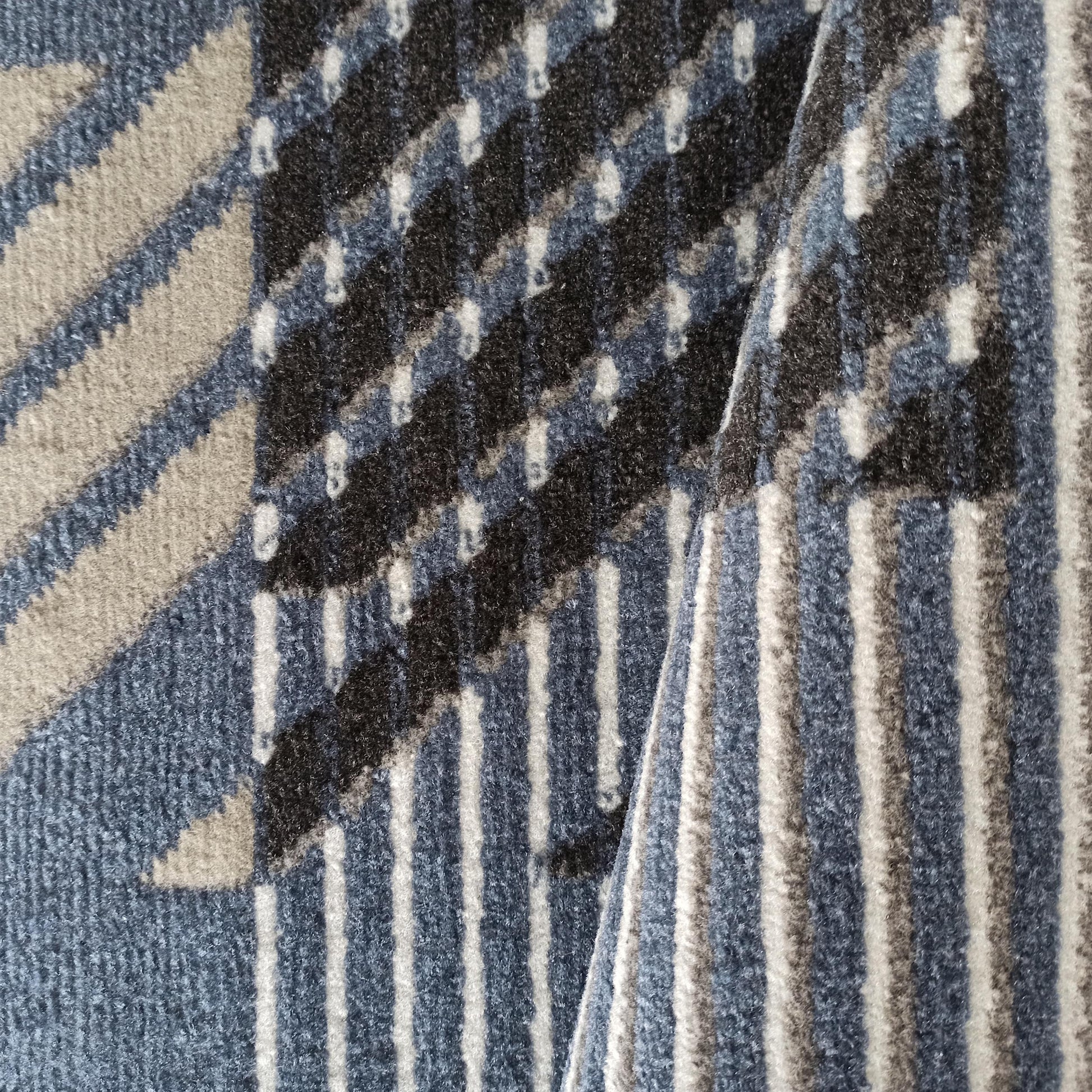 Tapis plié à texture douce avec des motifs géométriques et des rayures verticales, en teintes de bleu, gris, noir et blanc