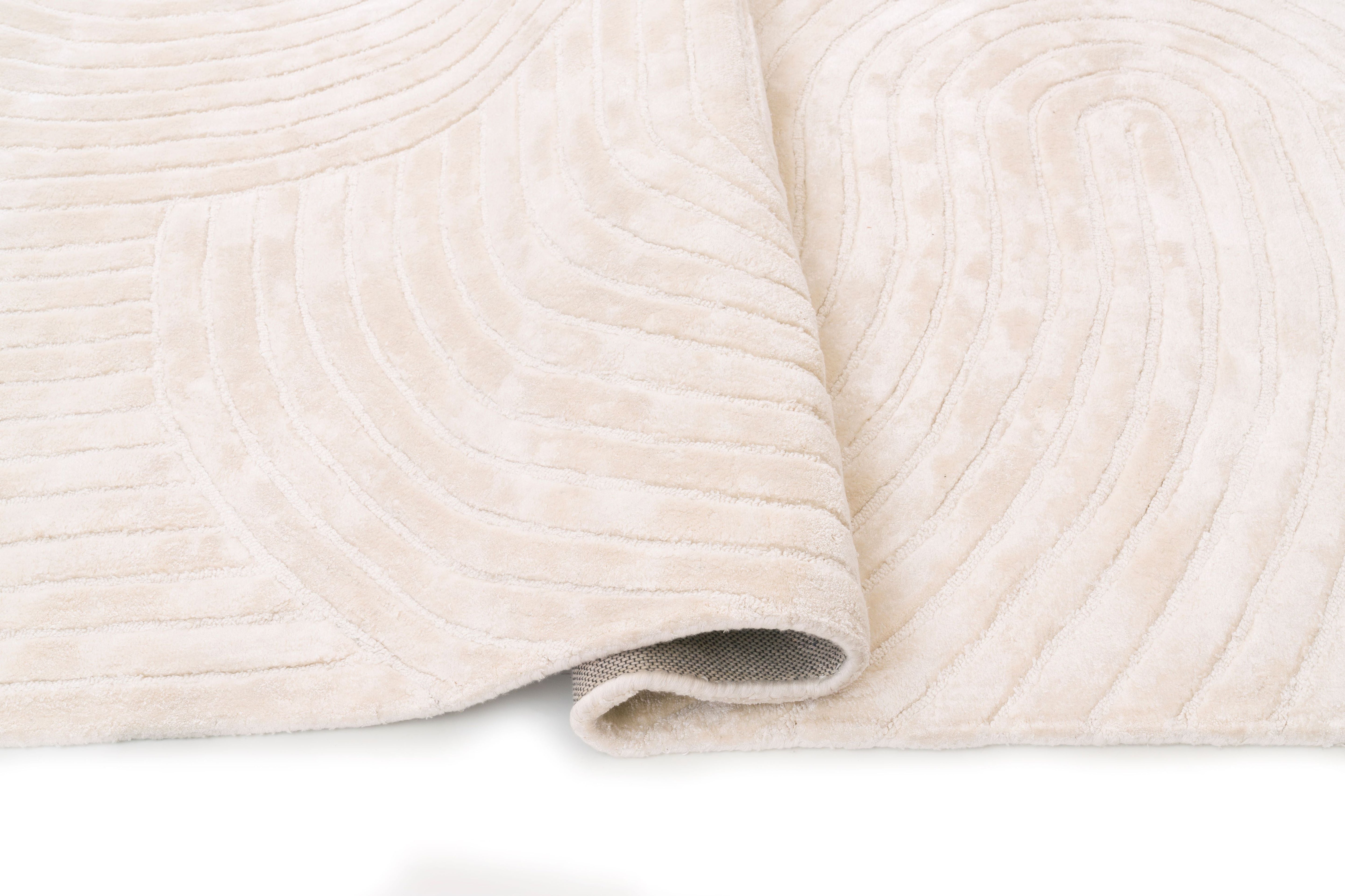 Tapis rectangulaire beige, dense et moelleux. Confort apparent grâce à la texture en relief. Ambiance chaleureuse