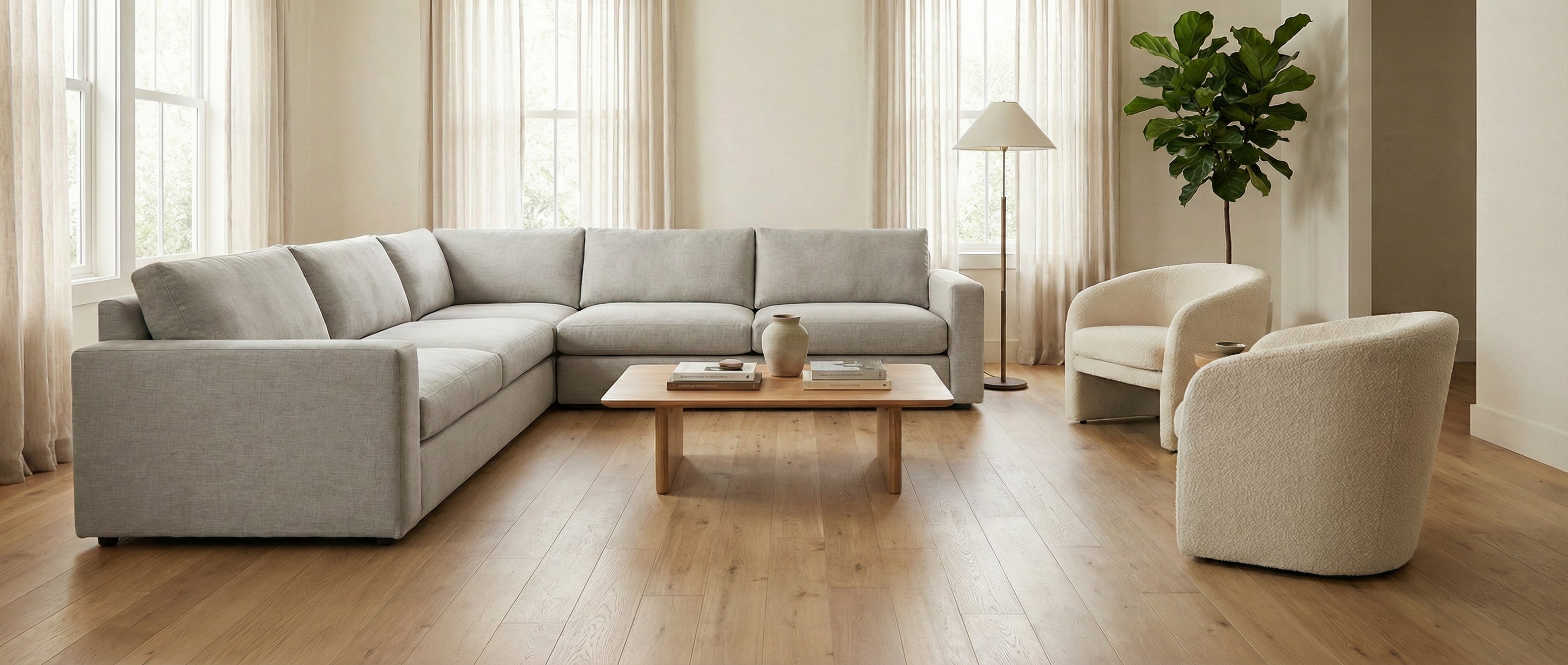 Pièce lumineuse avec canapé gris, fauteuils crème, parquet clair. Espace vide pour un tapis rectangulaire, ambiance