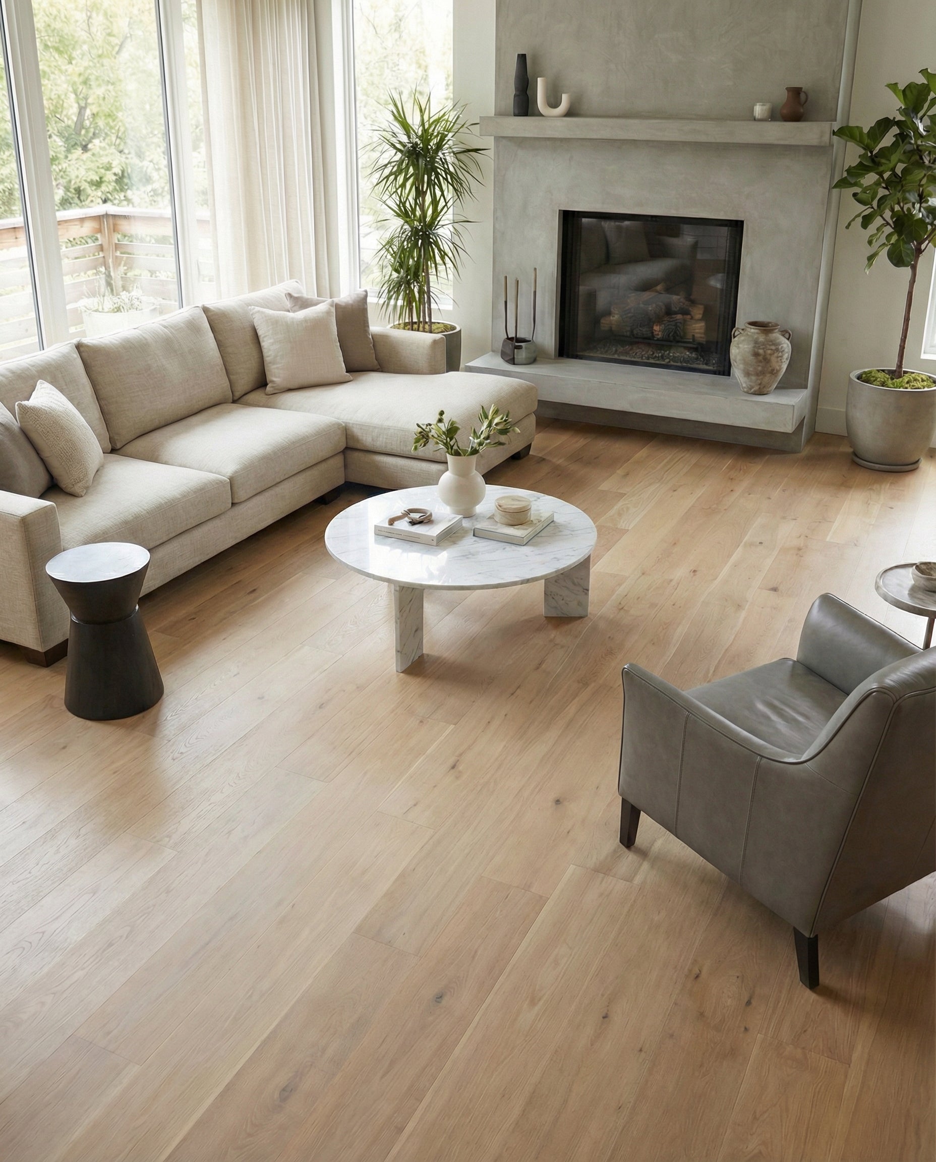 Pièce lumineuse avec plancher en bois clair, canapé beige, fauteuil gris, table ronde et cheminée