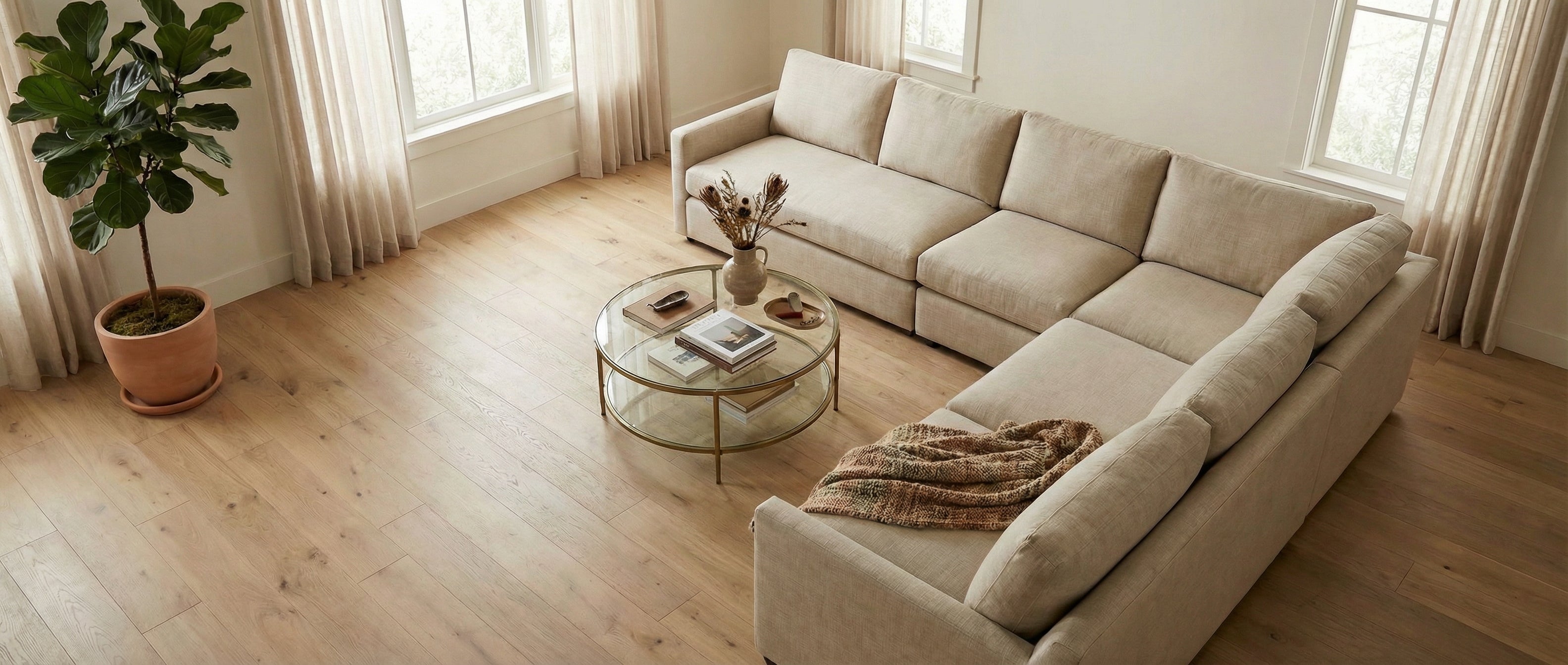 Pièce lumineuse aux murs blancs, parquet clair. Canapé taupe, table ronde. Espace vide, potentiel déco