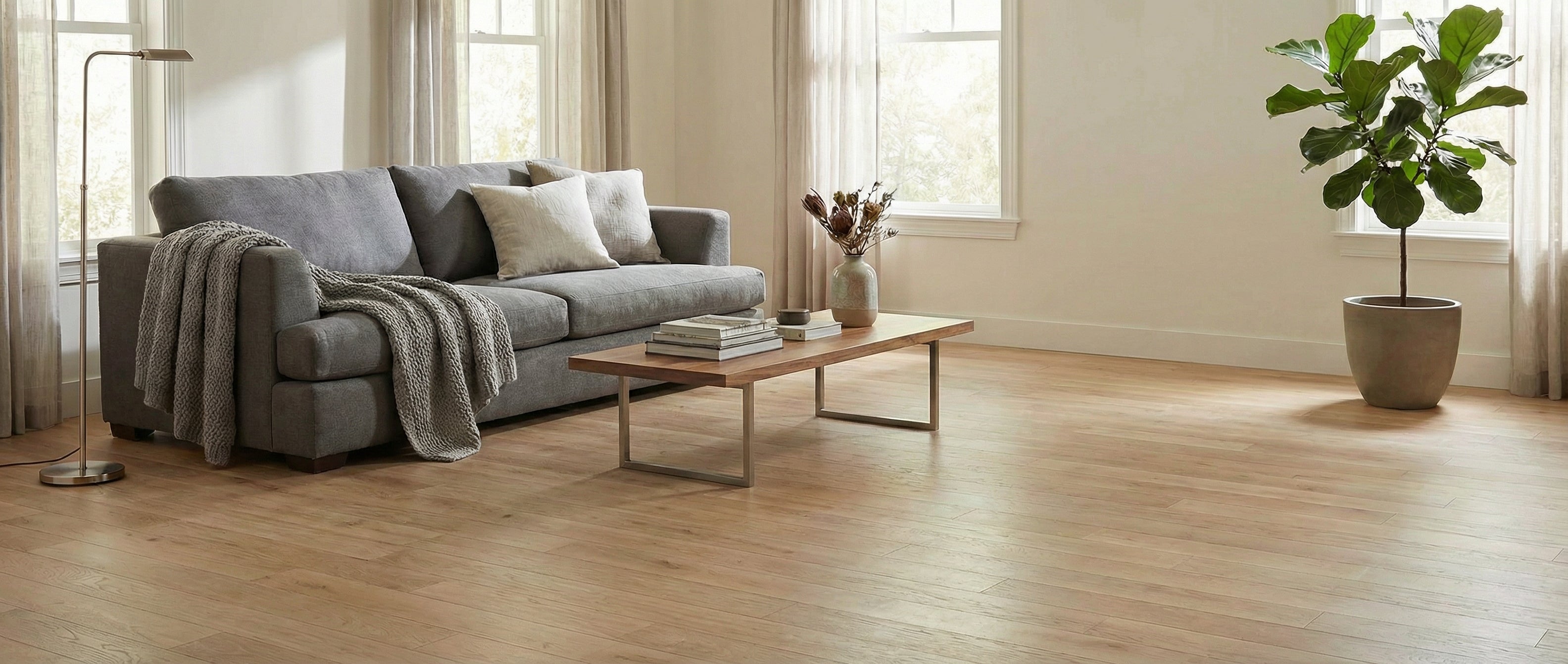 Pièce avec plancher de bois clair, canapé gris, table basse. Espace à transformer pour un tapis rond