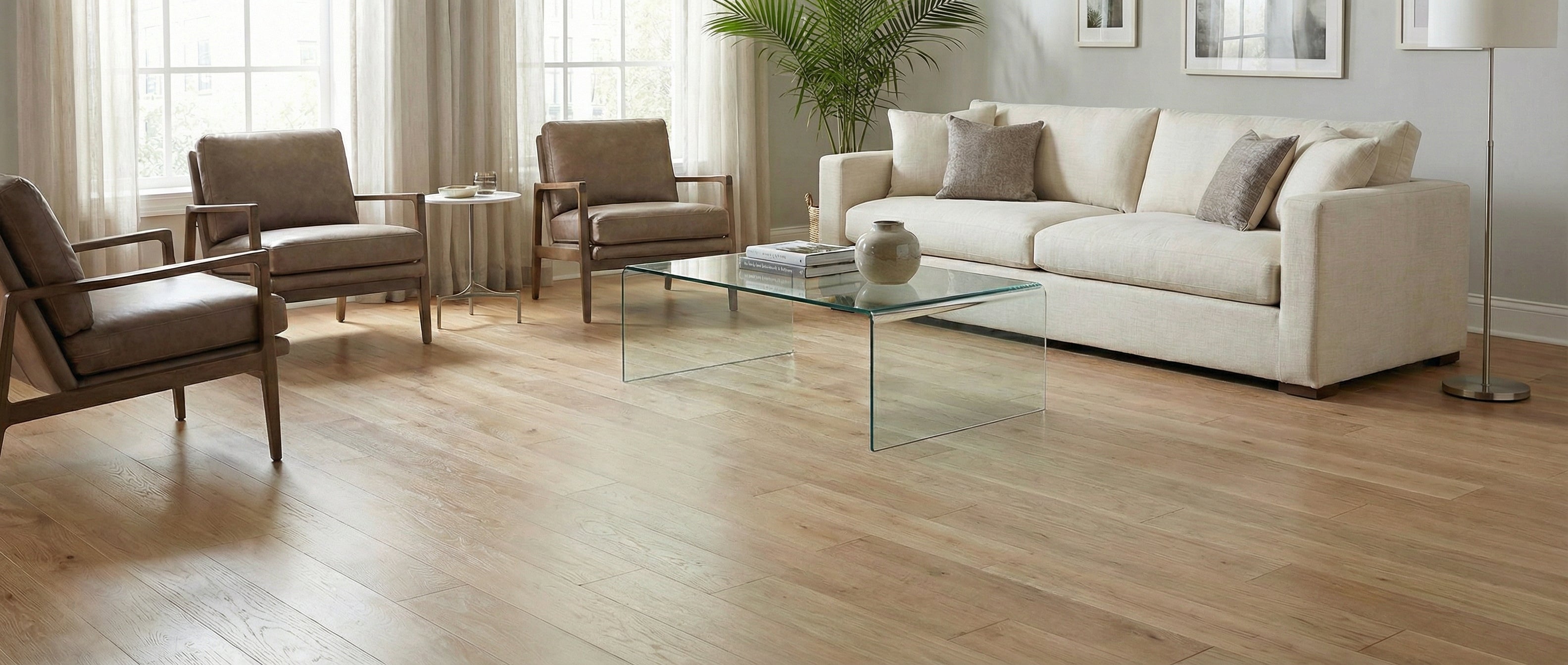 Pièce avec plancher en bois clair, sans tapis. Espace à transformer. Canapé et fauteuils gris. Table basse en verre