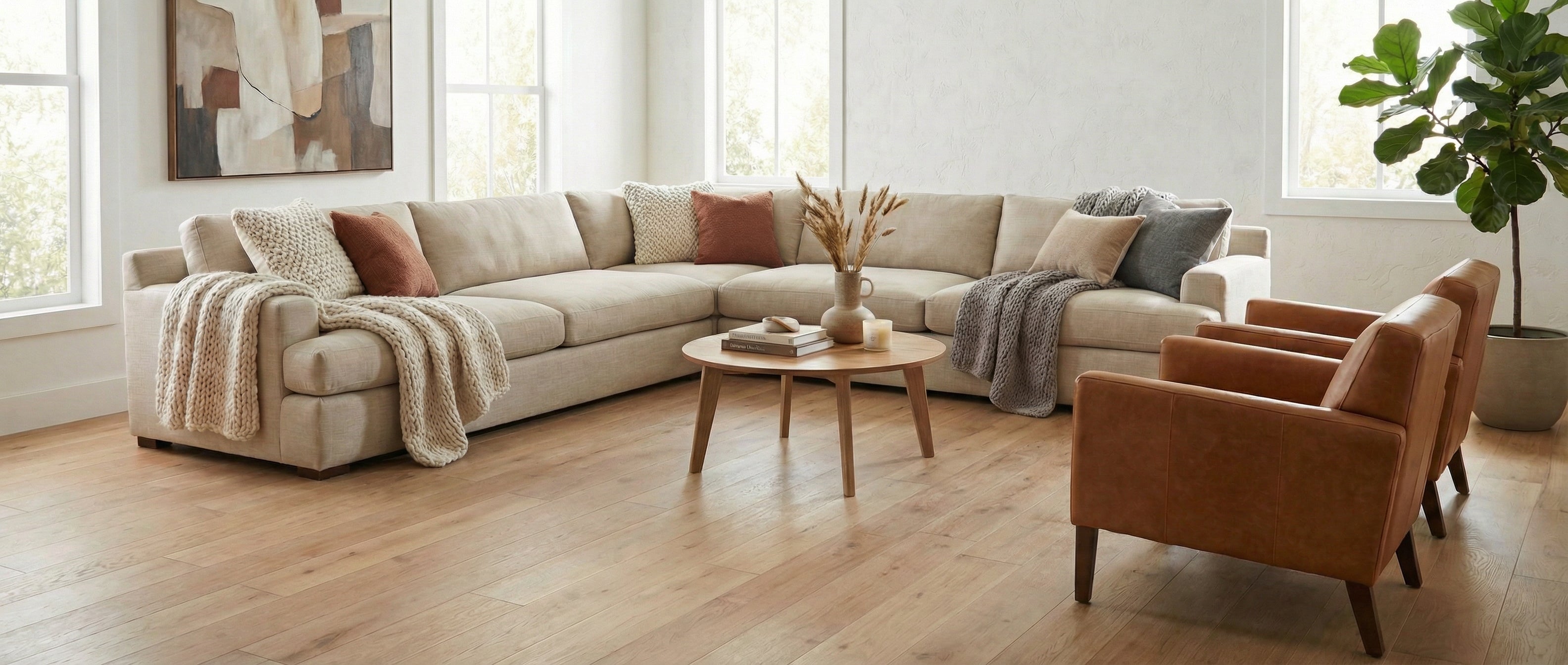 Pièce lumineuse avec canapé beige, fauteuils cuir. Sol bois clair. Table ronde. Espace pour tapis