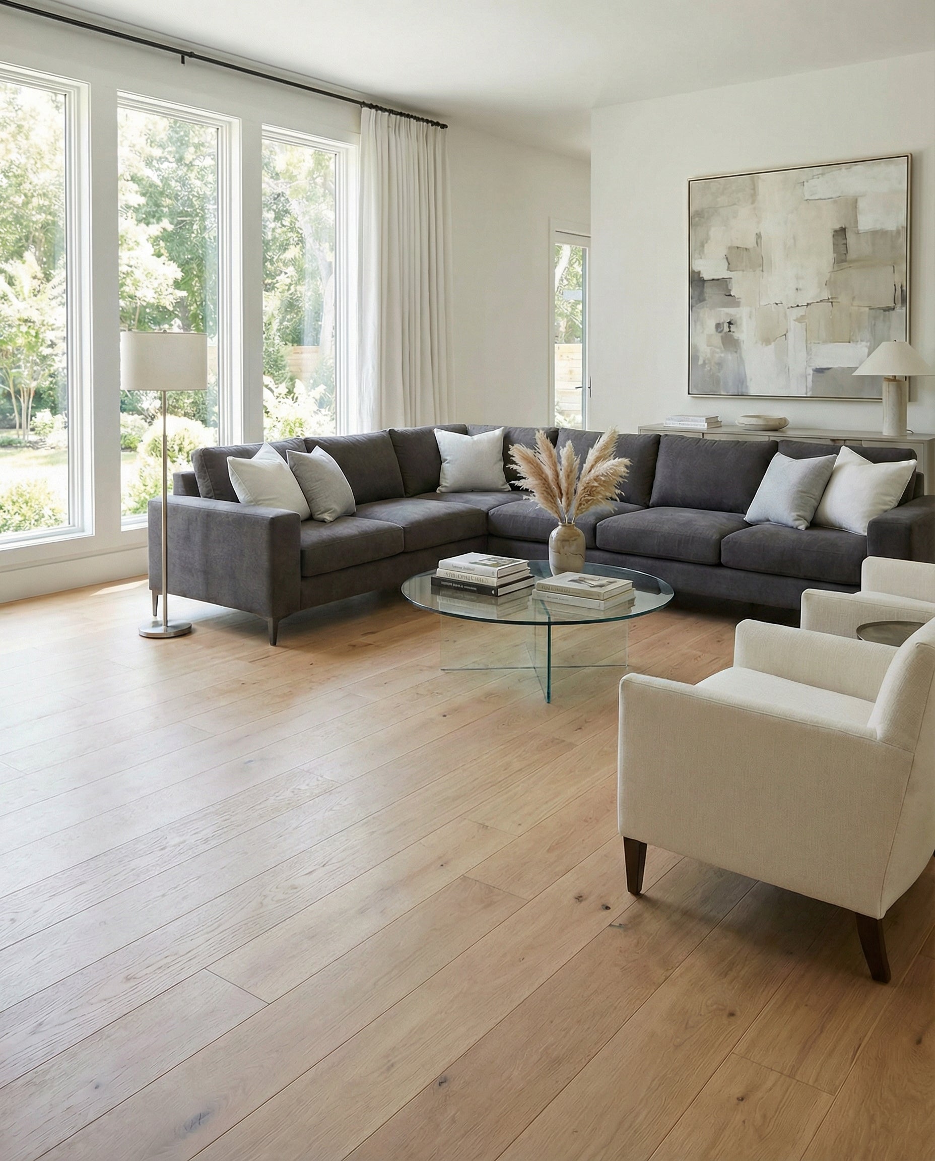 Pièce lumineuse avec parquet clair. Canapé gris, fauteuils beiges. Table basse ronde en verre. Ambiance épurée et moderne