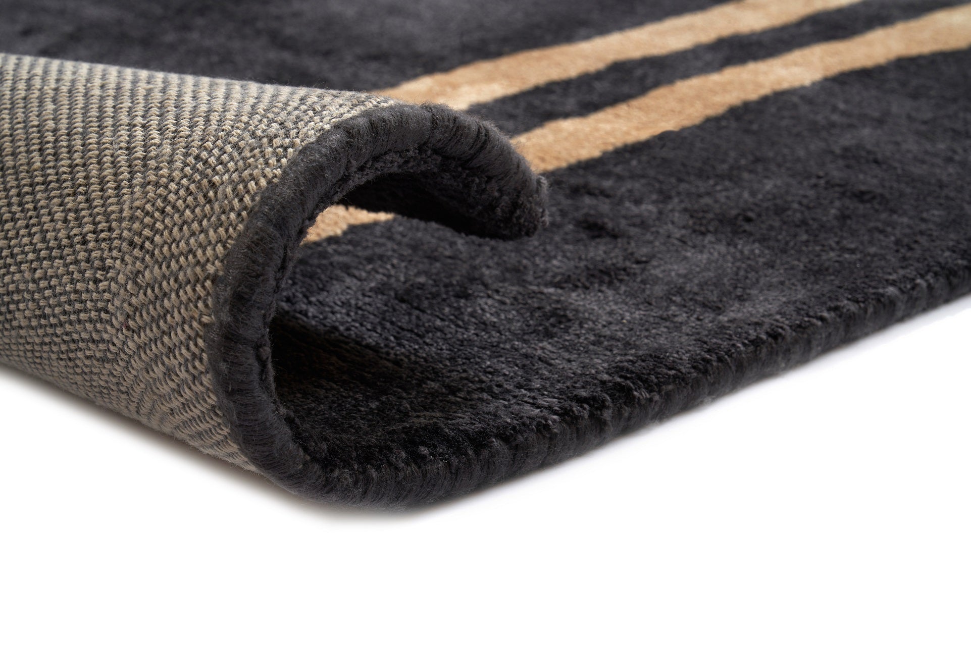 Bordure noire cousue sur un tapis rectangulaire. Dos tissé beige. Deux bandes dorées sur fond noir. Finition de qualité