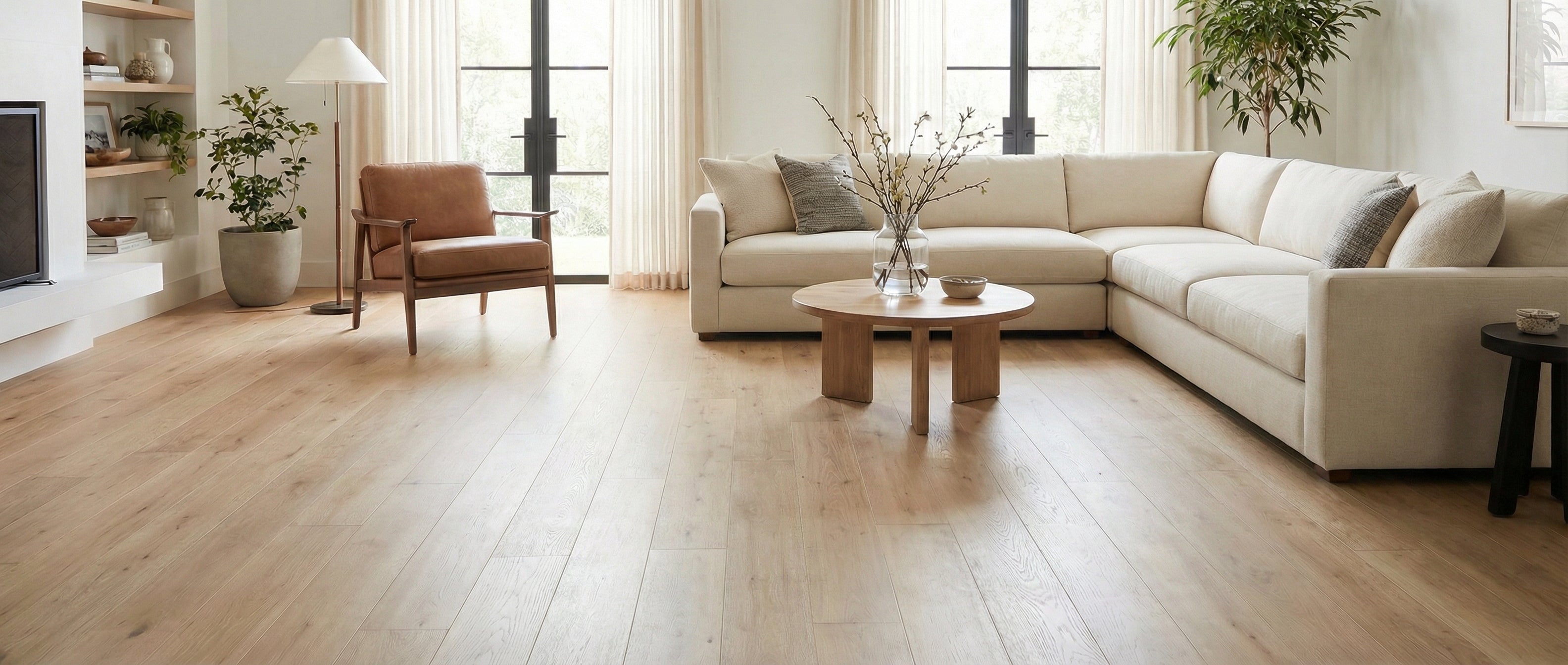 Pièce lumineuse avec parquet clair, canapé beige, fauteuil cuir, table basse ronde. Espace vide pour un tapis