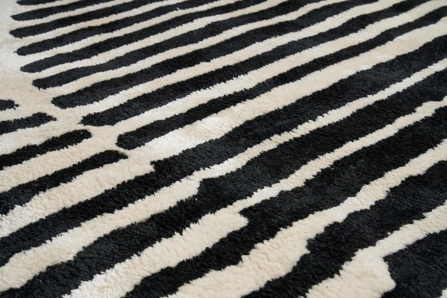 Tapis à rayures noires et ivoire, tissage touffeté. Relief doux et texturé, aspect tactile. Ambiance chaleureuse