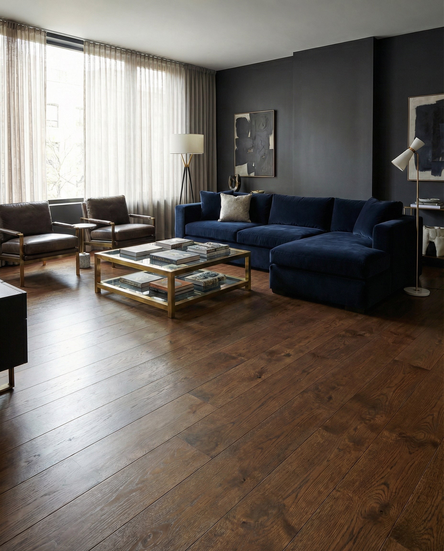 Pièce avec parquet marron, canapé bleu, murs gris foncé, fauteuils en cuir, table basse dorée, ambiance moderne