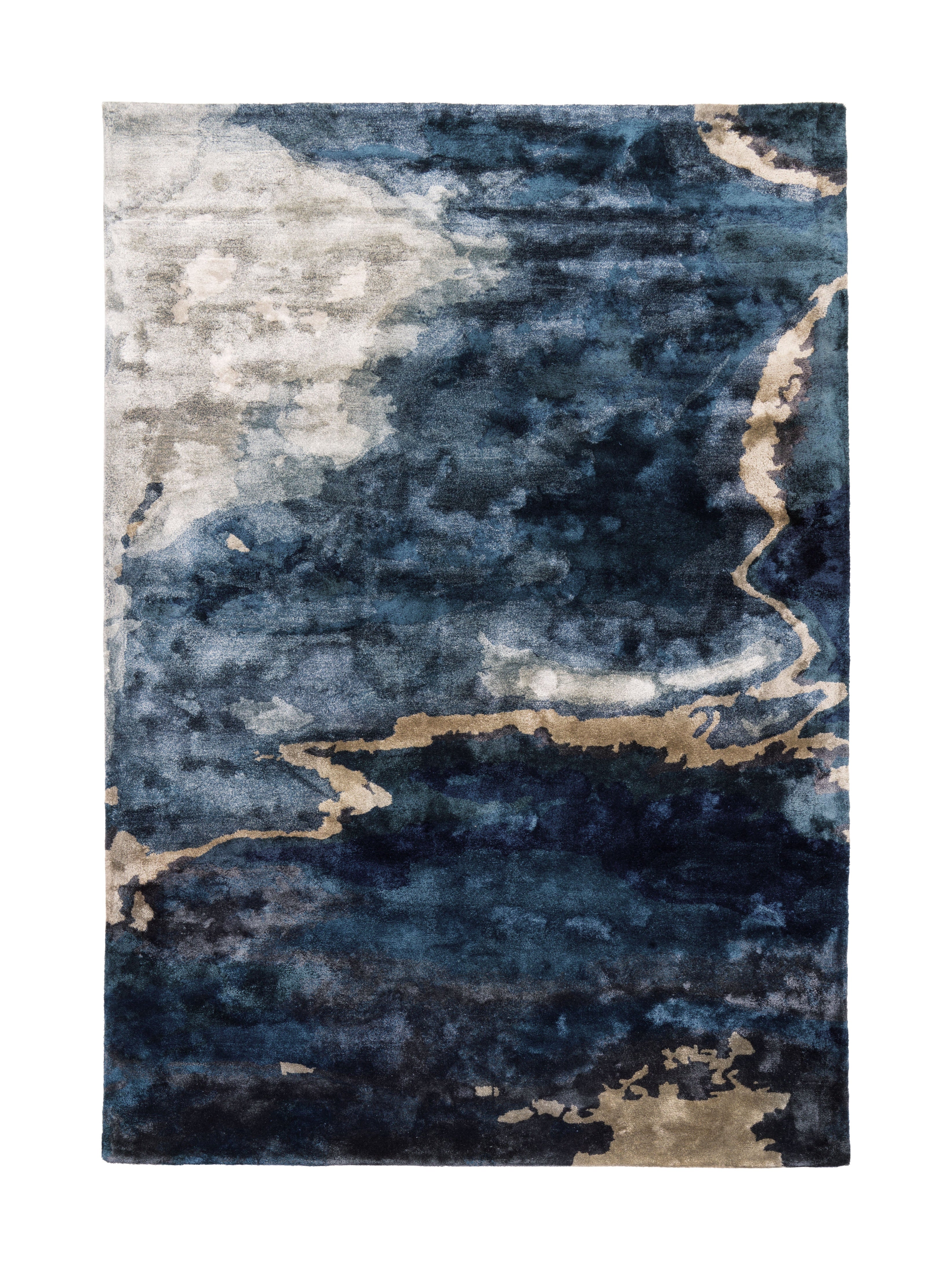 Tapis rectangulaire avec motif abstrait. Les couleurs principales sont le bleu, le beige et le gris, créant une ambiance