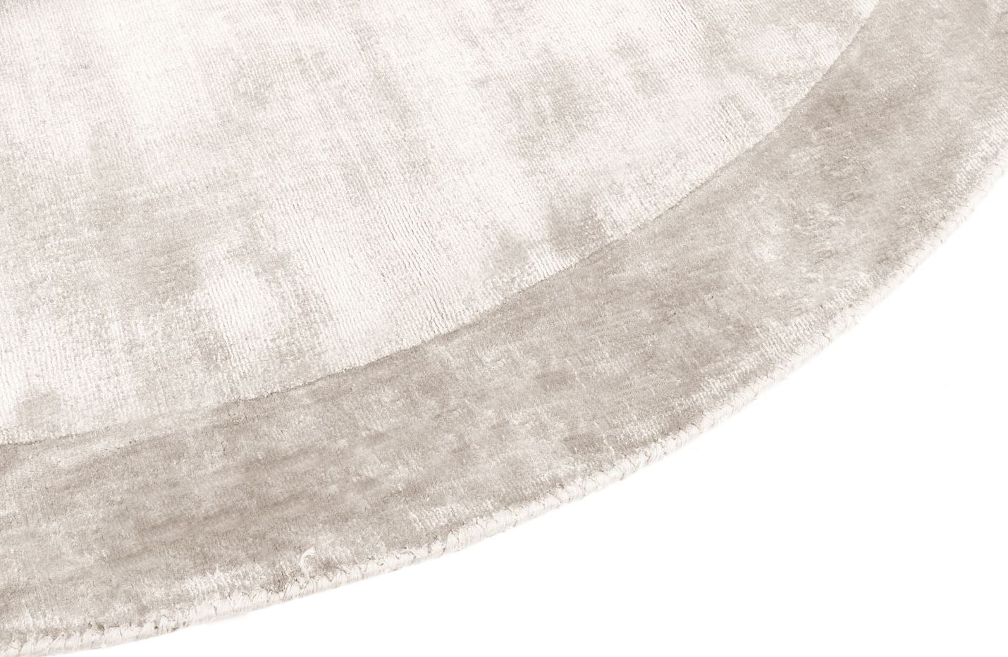 Tapis rond argenté, tissage texturé, relief subtil. Aspect tactile doux et velouté. Ambiance feutrée