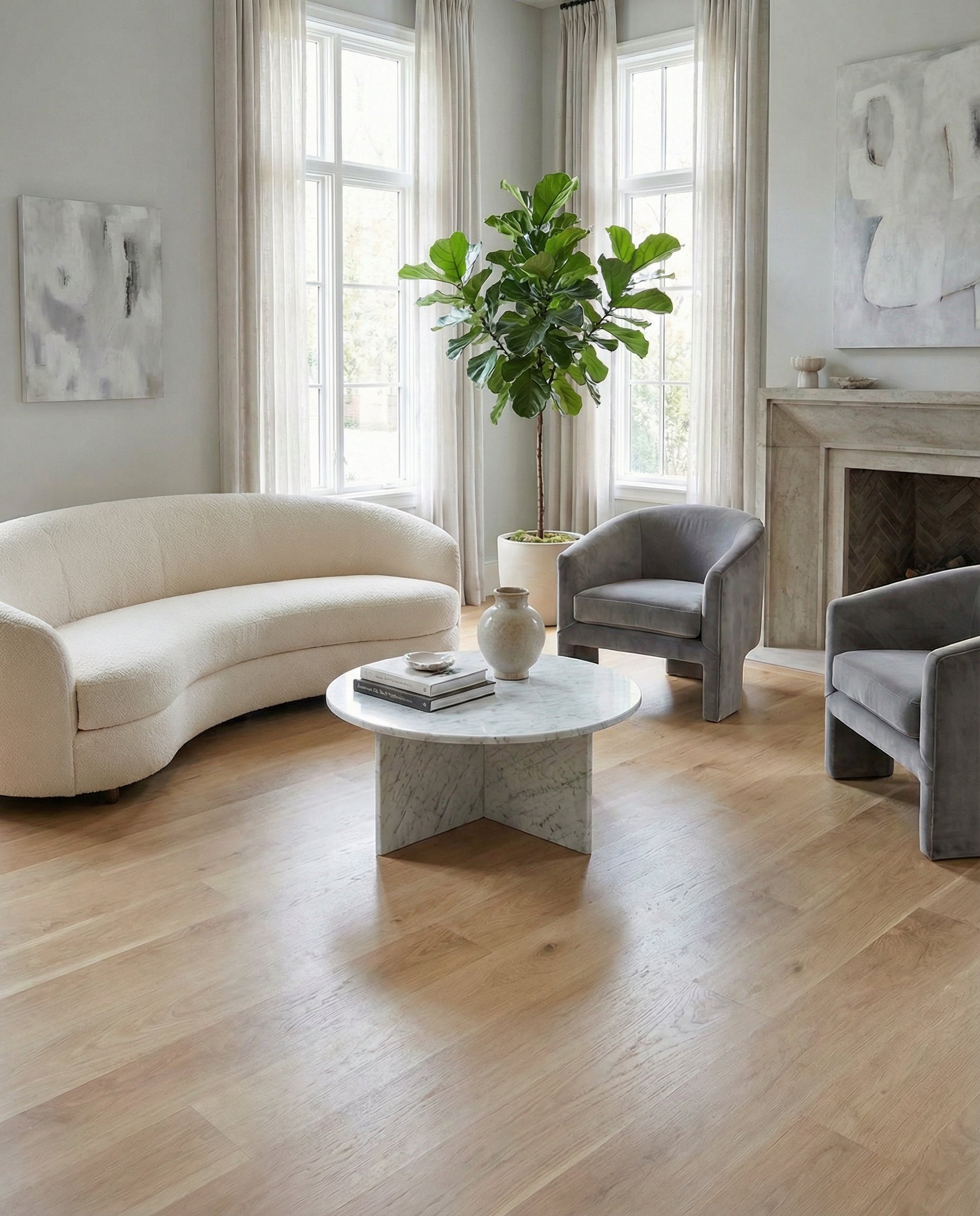 Pièce lumineuse, ambiance neutre, parquet clair. Canapé crème, fauteuils gris. Table ronde marbre, vase. Fenêtres,