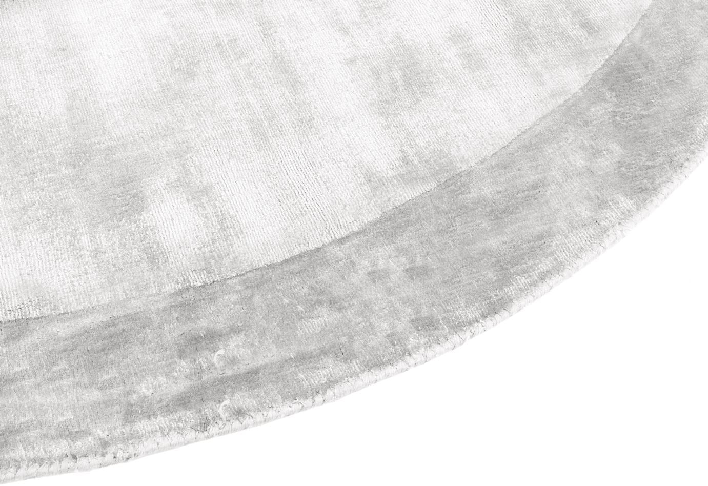 Gros plan sur un tapis rond. Tissage velours avec relief et aspect tactile. Couleurs gris et perle. Ambiance feutrée