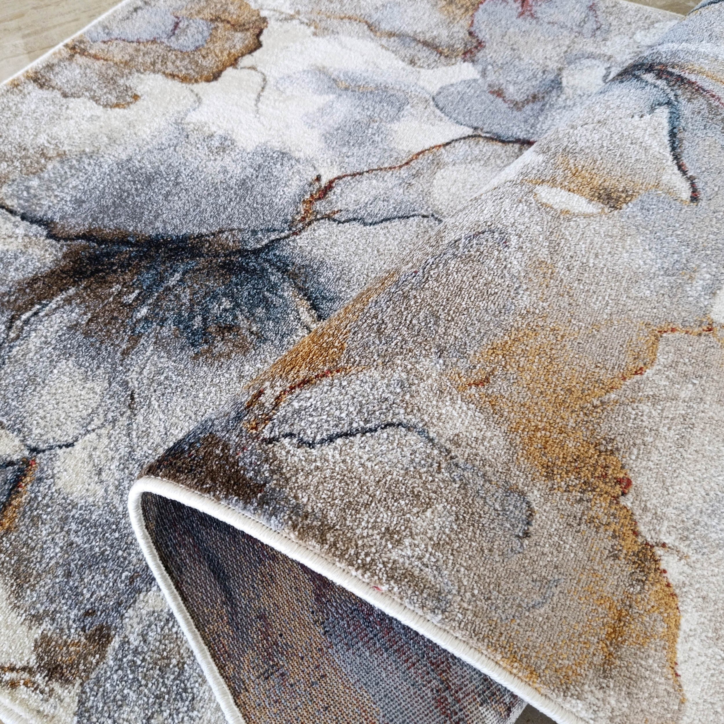 Tapis abstrait gris, beige, marron et bleu aux lignes sombres et rouille, partiellement roulé, bordure crème
