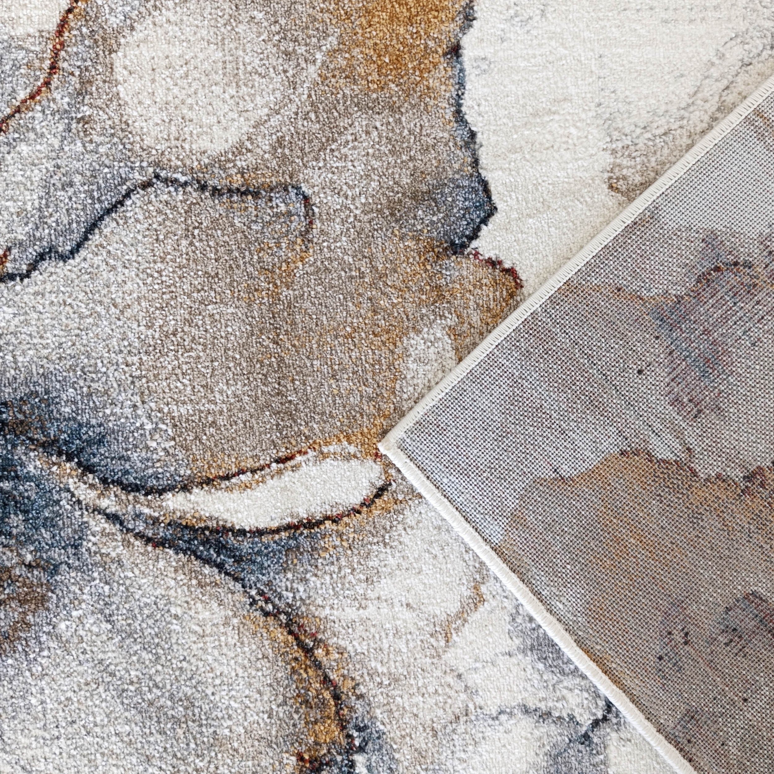 Dessus texturé d'un tapis aux motifs abstraits crème, marron, gris et bleu, avec son envers quadrillé beige clair replié