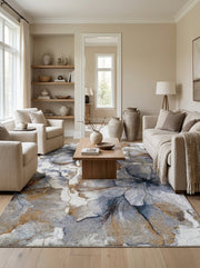 Tapis rectangulaire à motifs floraux abstraits bleus, gris, blancs et dorés, posé sur un parquet clair dans un salon