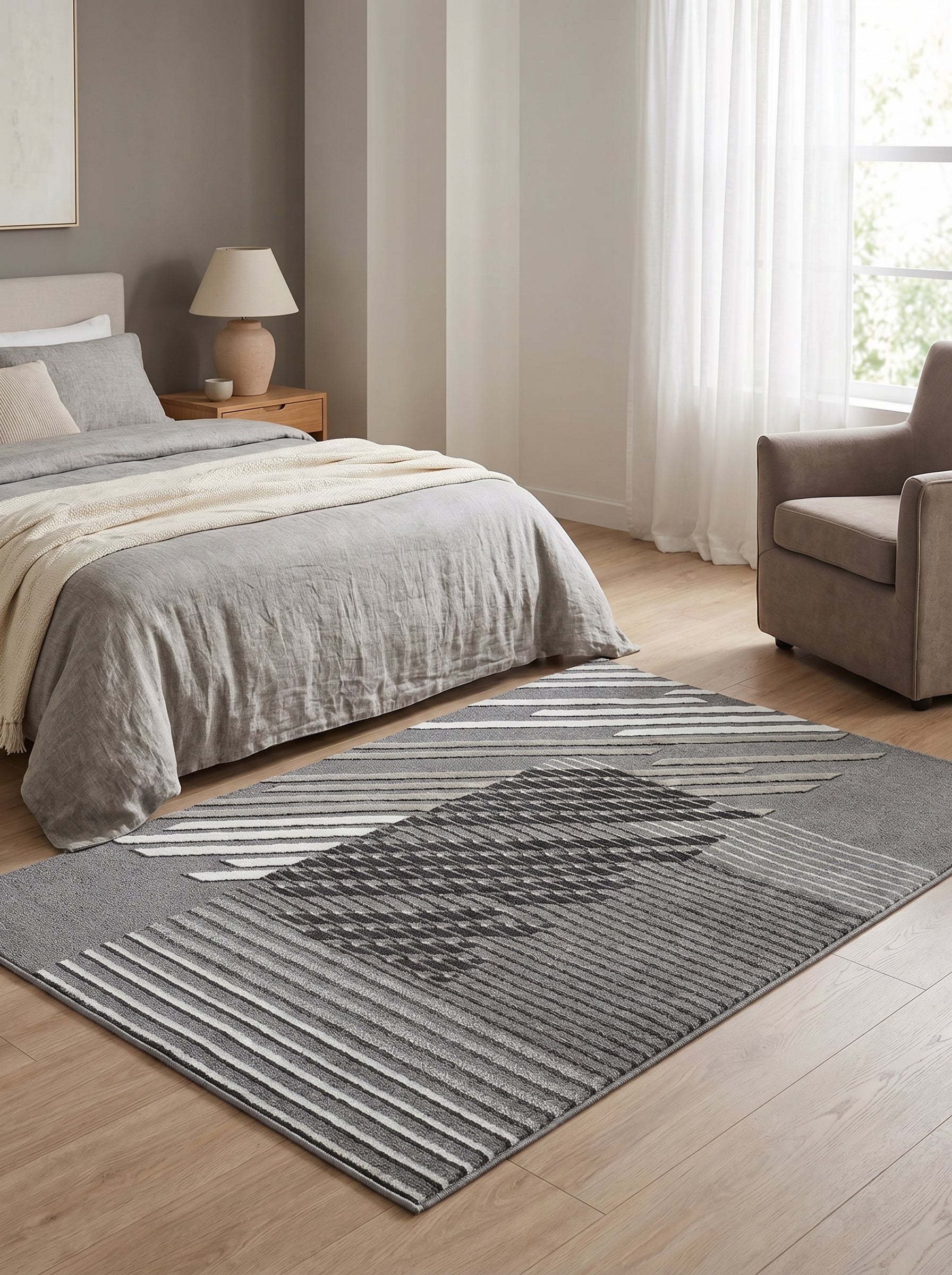 Tapis gris à poils courts, aux motifs géométriques abstraits combinant des rayures claires et des blocs gris foncés, dans une chambre