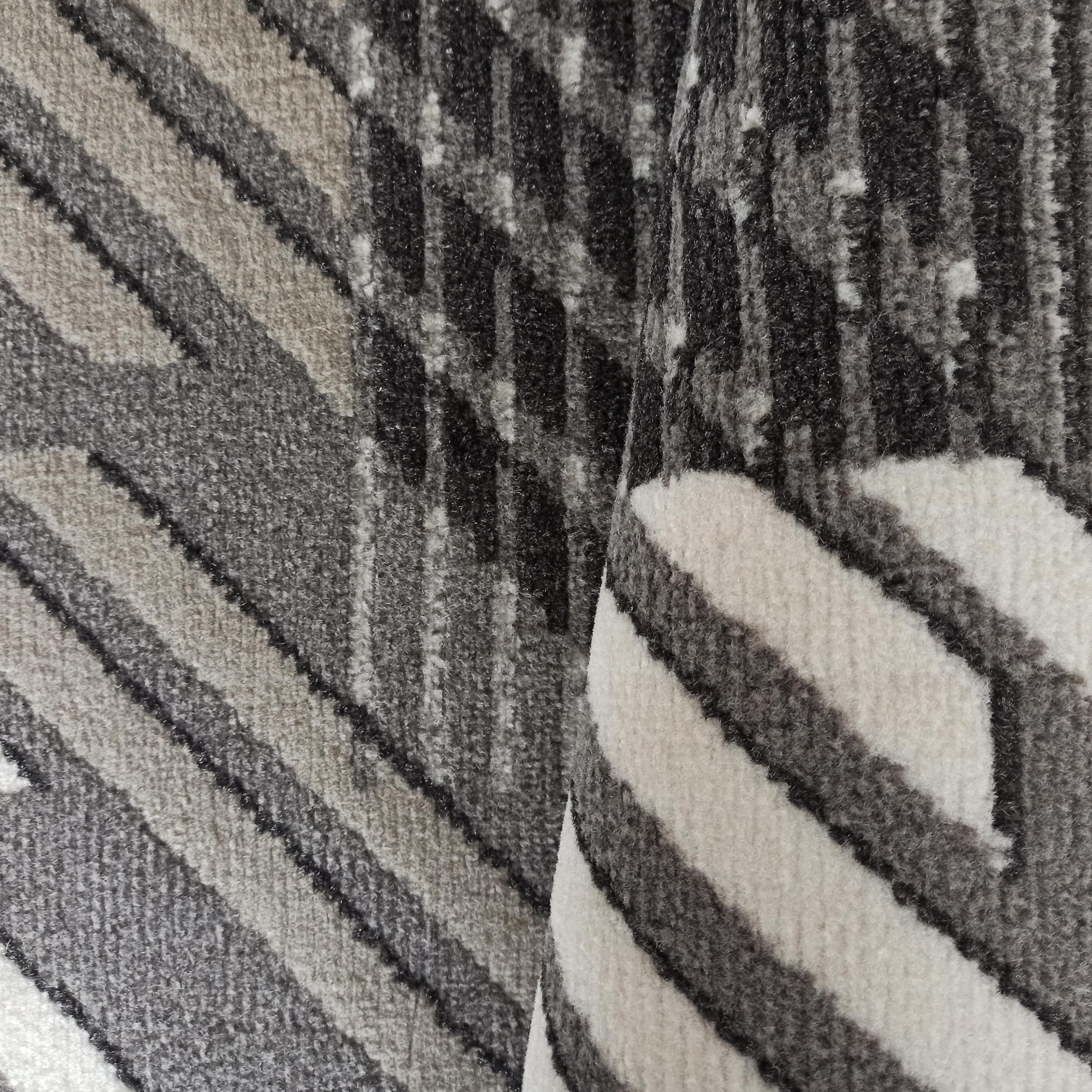 Tapis moelleux et replié, orné d'un motif abstrait géométrique de bandes et formes irrégulières en gris, blanc et noir