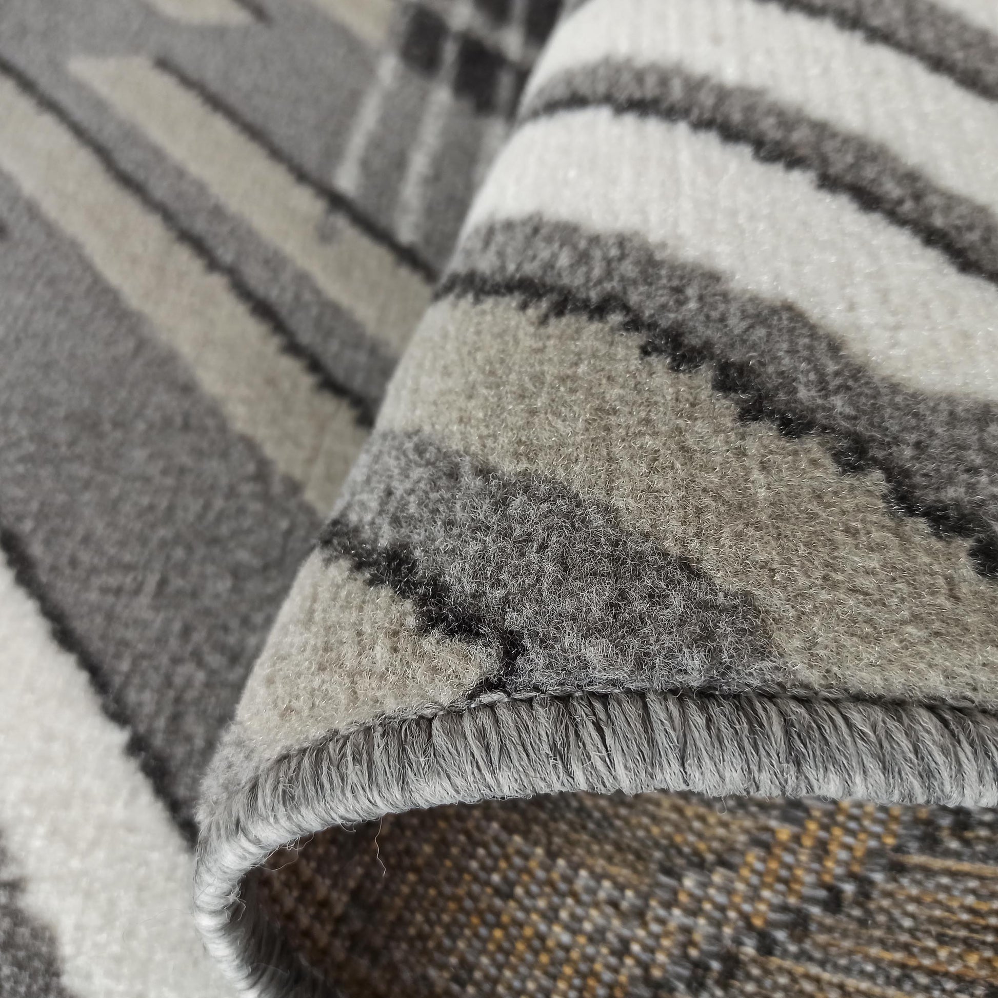 Gros plan d'un tapis moelleux enroulé aux motifs abstraits gris, blancs et noirs. Le revers tissé est teinté de jaune et brun