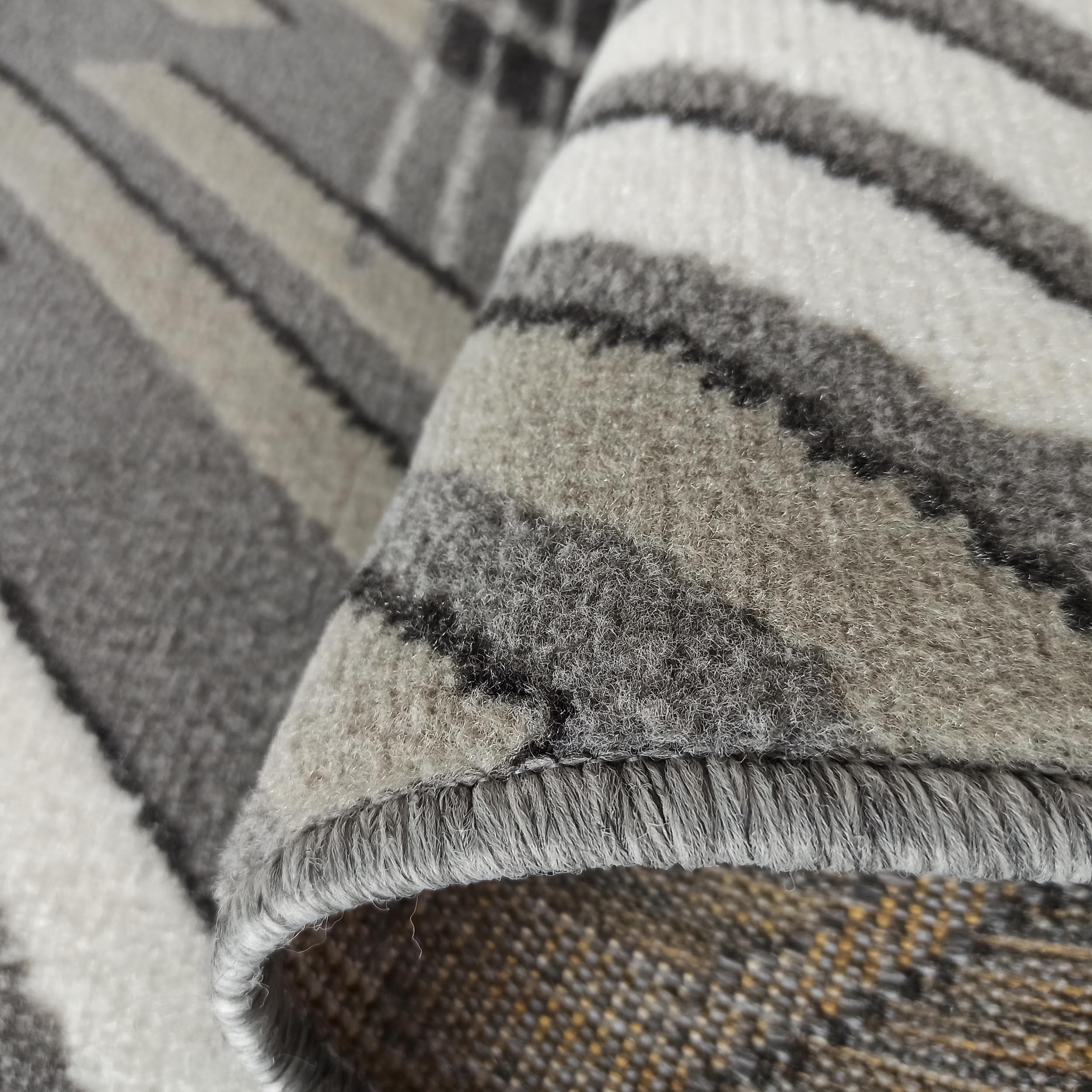 Gros plan d'un tapis moelleux enroulé aux motifs abstraits gris, blancs et noirs. Le revers tissé est teinté de jaune et brun
