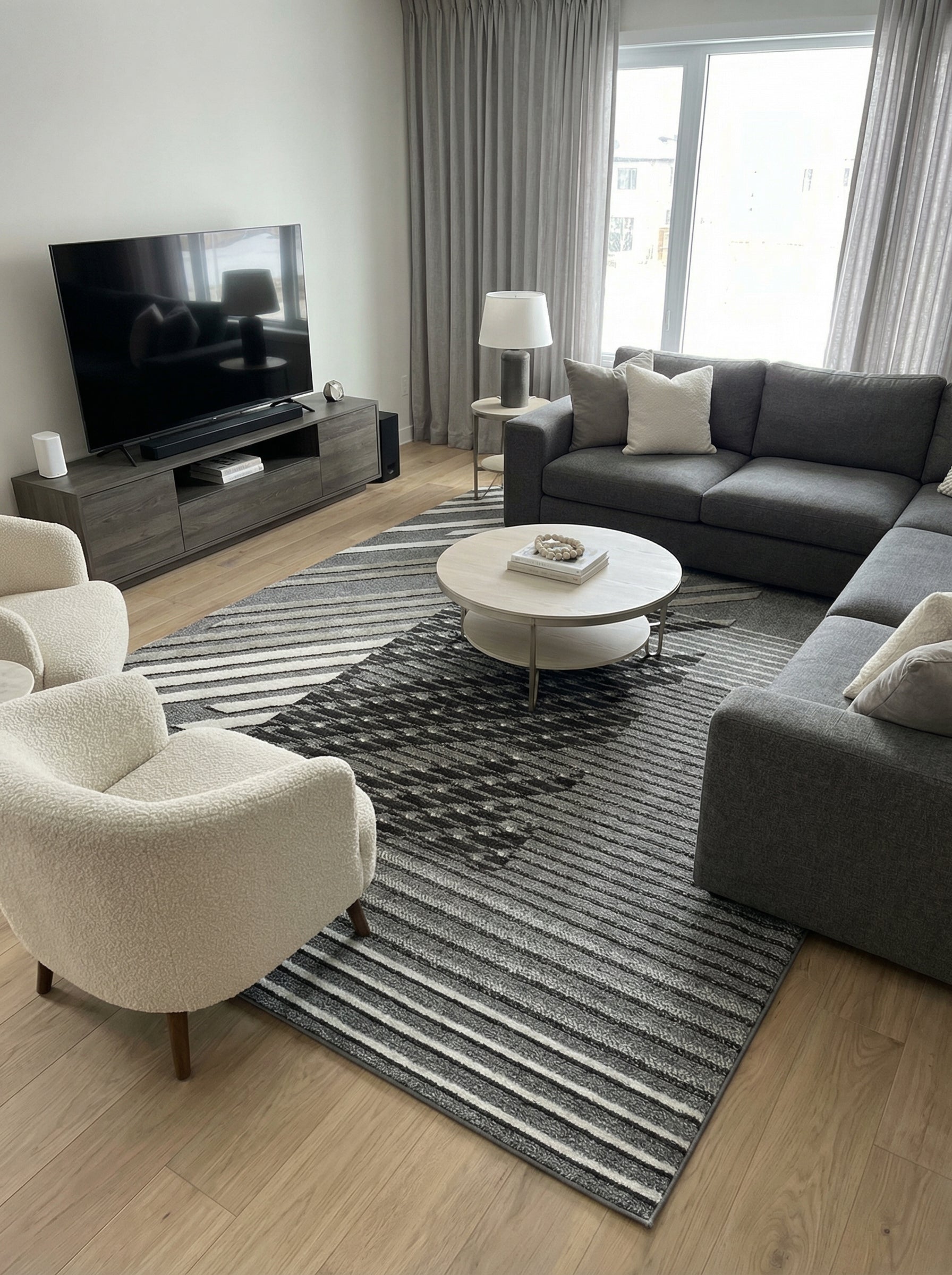 Tapis moderne aux motifs géométriques gris, noirs et blancs avec des rayures convergentes et une section texturée au centre, dans un salon