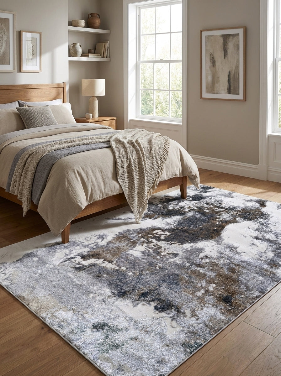 Tapis rectangulaire aux motifs abstraits gris foncé, bleu, brun et blanc cassé sur un parquet de chambre